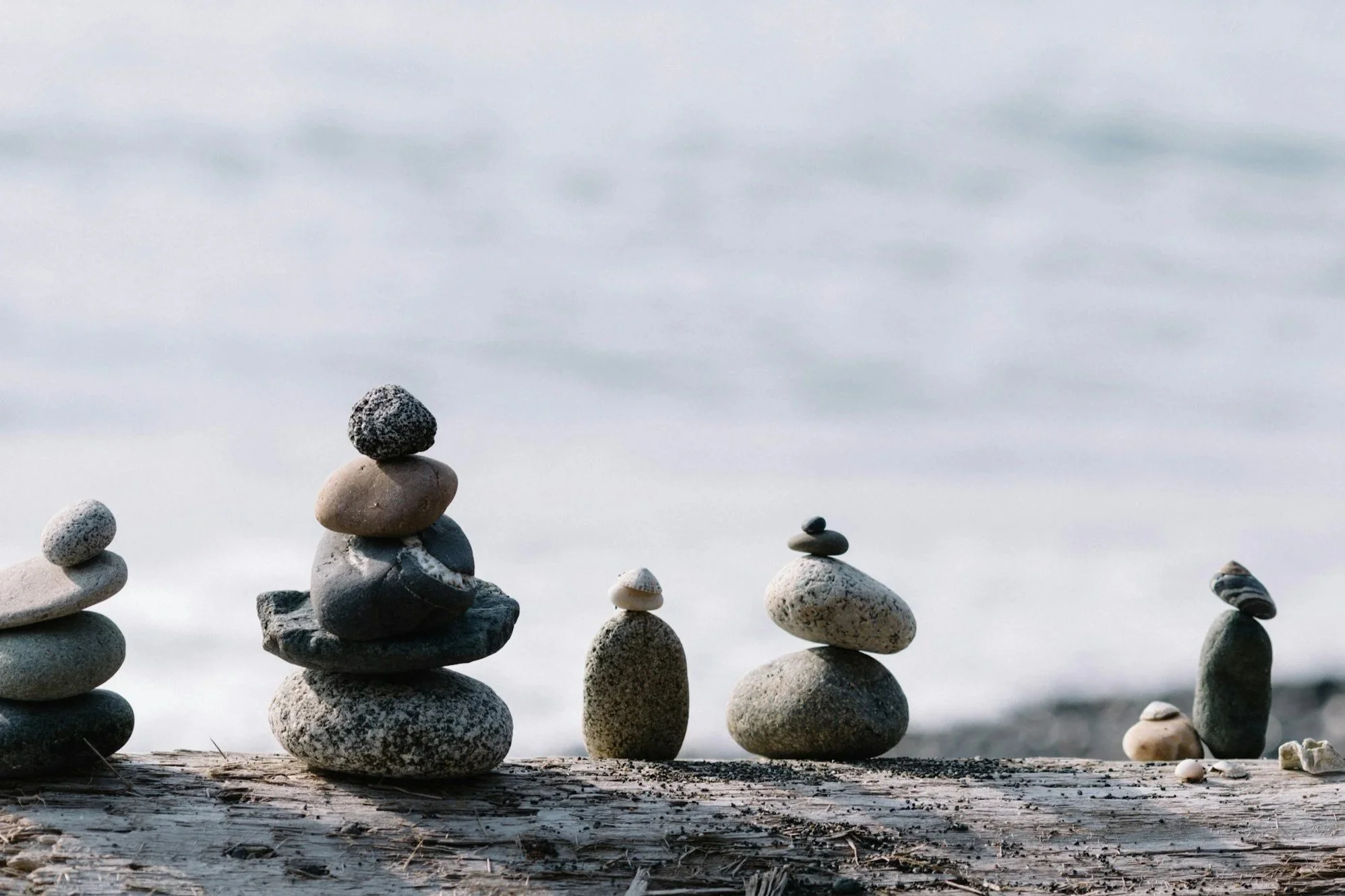 Several stacks of smooth, rounded rocks of various sizes and colors placed on a weathered wooden surface, with a calm, cloudy sky in the background.