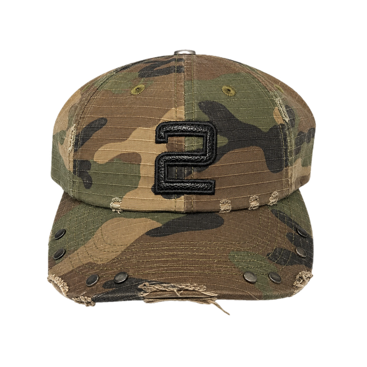 Camouflage baseball cap with a large black embroidered number two on the front, distressed brim with metal eyelets and frayed edges.