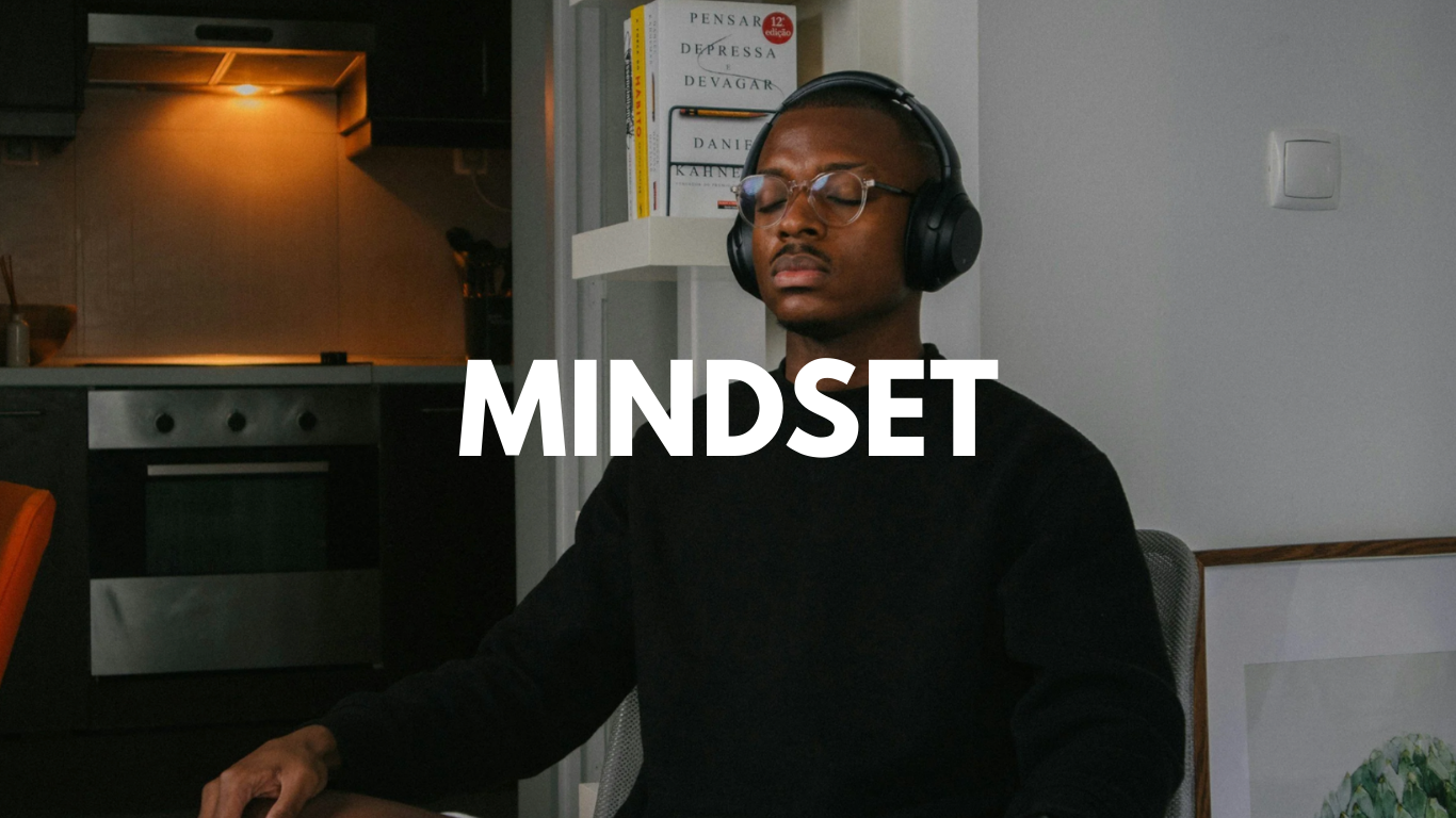 A young man with glasses and headphones sitting with his eyes closed, meditating or relaxing at home, with the word "MINDSET" overlaid on the image.