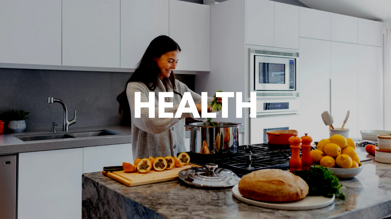 A woman cooking in a modern kitchen with various fruits, bread, and vegetables on the counter.