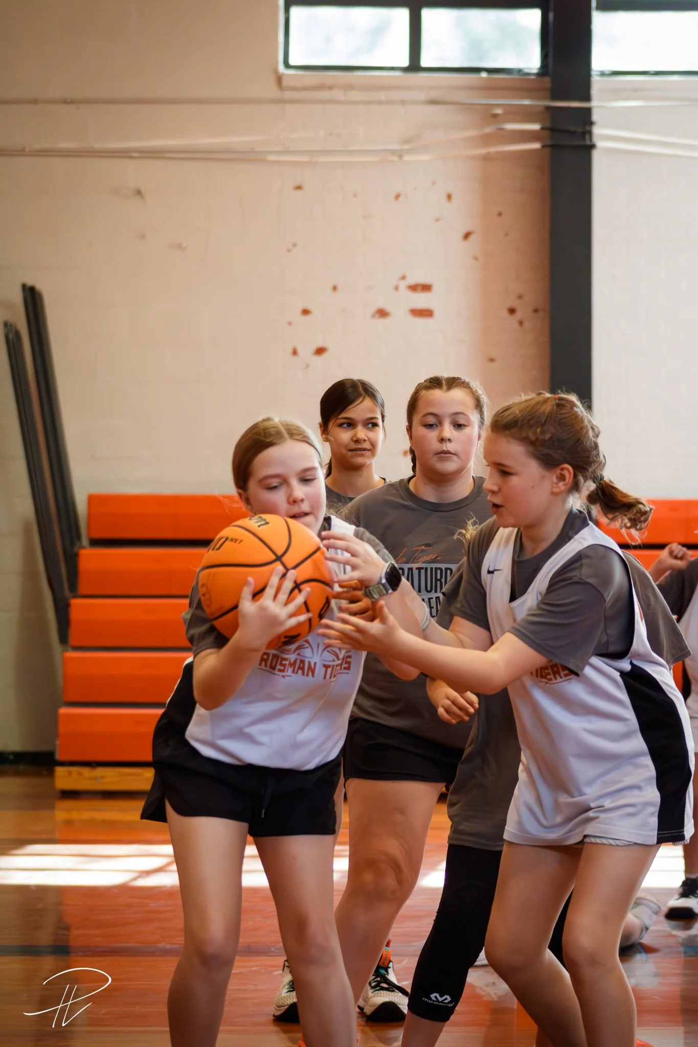 Girls practicing basketball in gymnasium with coach supervising.