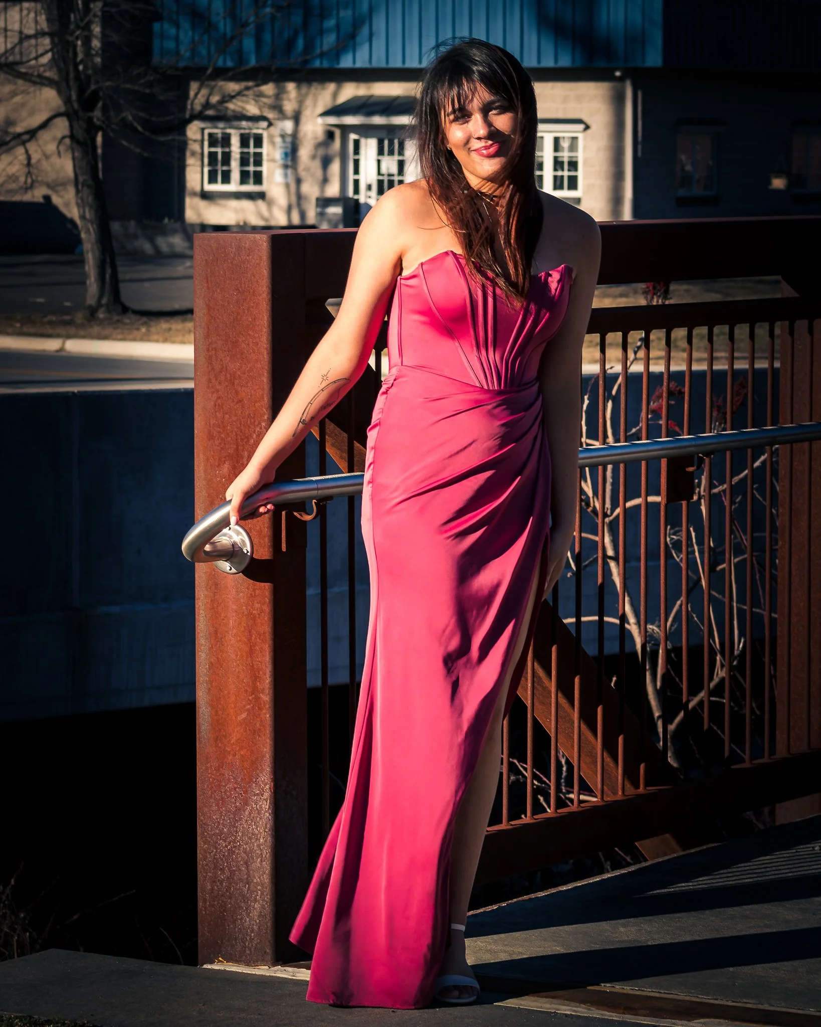 Woman in a pink strapless gown standing on a bridge railing.