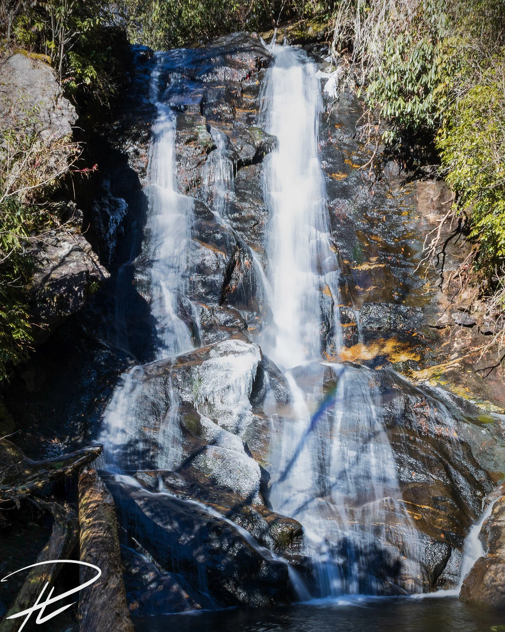 Waterfall flowing over rocks surrounded by greenery in a forest.