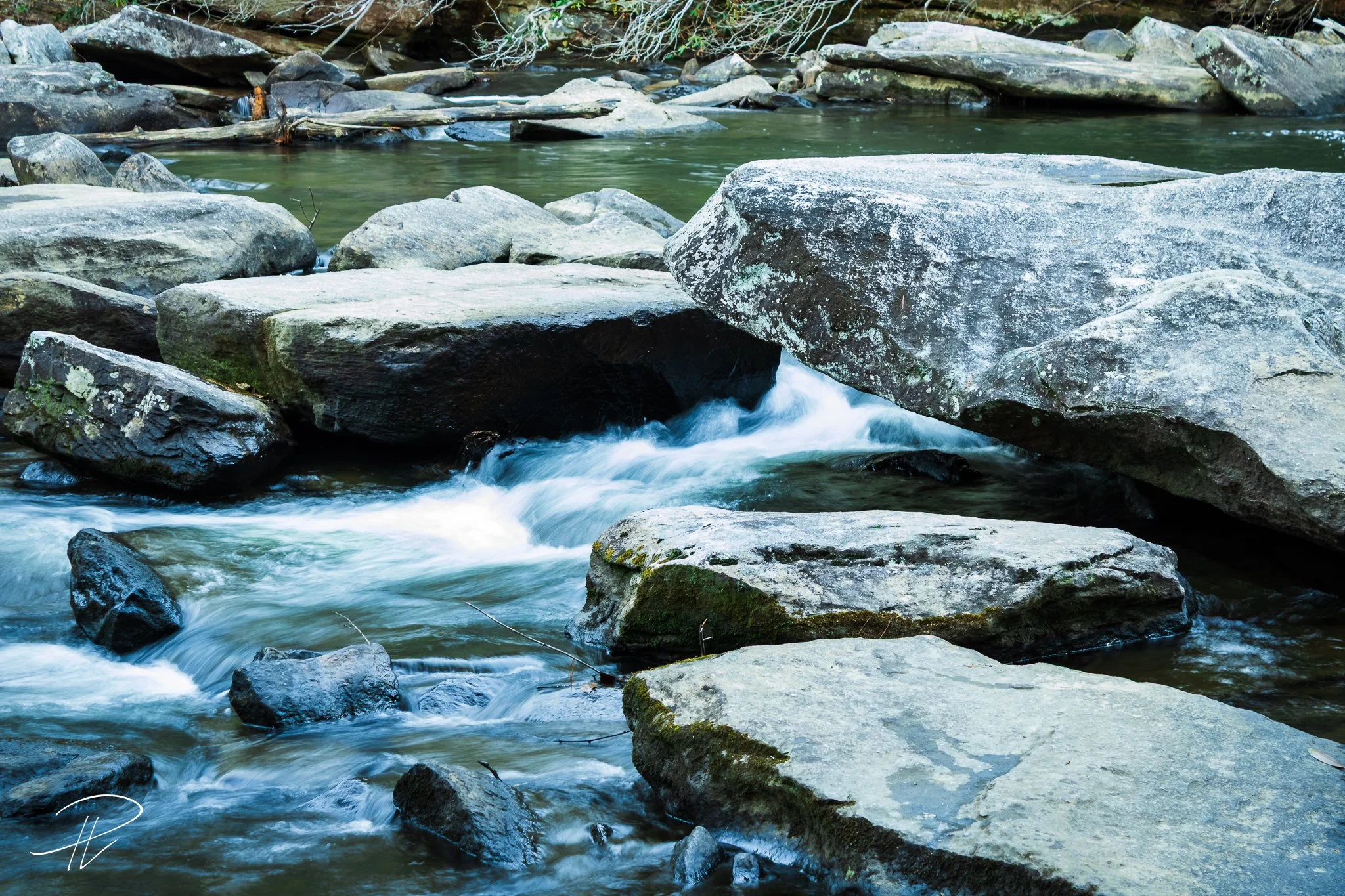 A close-up view of a shallow stream flowing over rocks and stones in a natural outdoor setting.