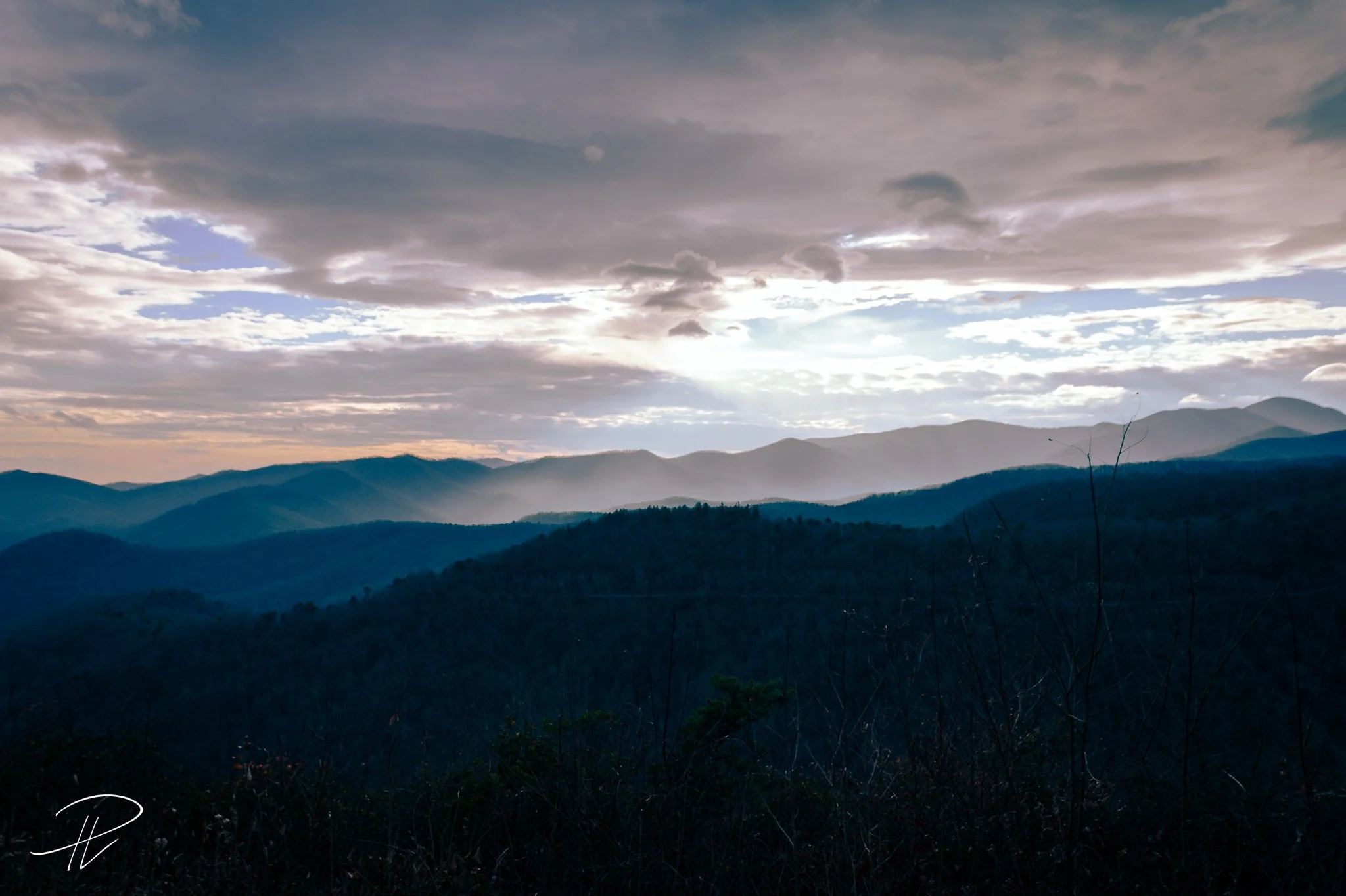 Landscape of mountain range under a cloudy sky with sunlight breaking through the clouds.