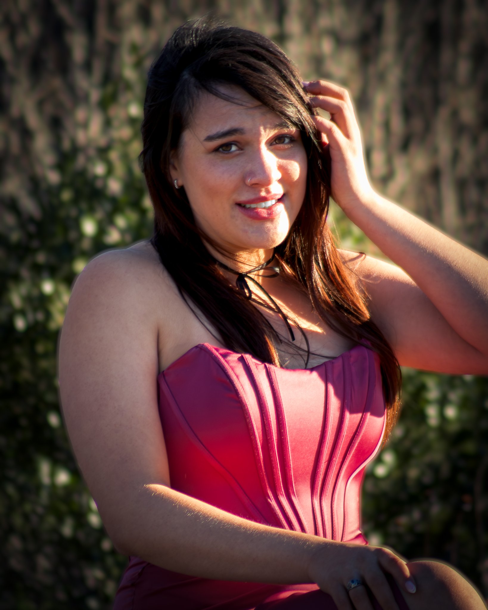 A woman with dark brown hair in a pink strapless dress outdoors.