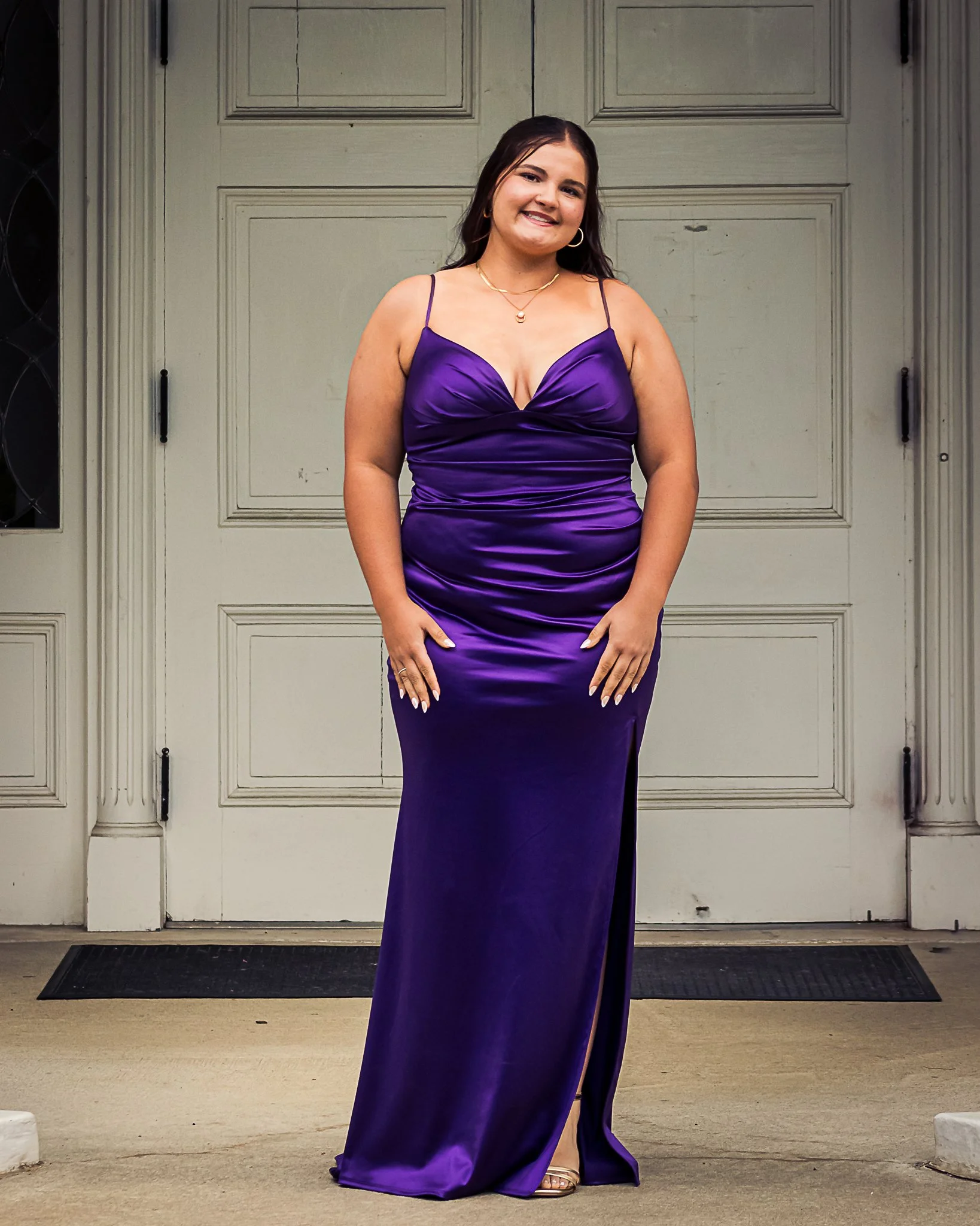 A woman in a purple satin evening gown standing in front of a white garage door, smiling at the camera.