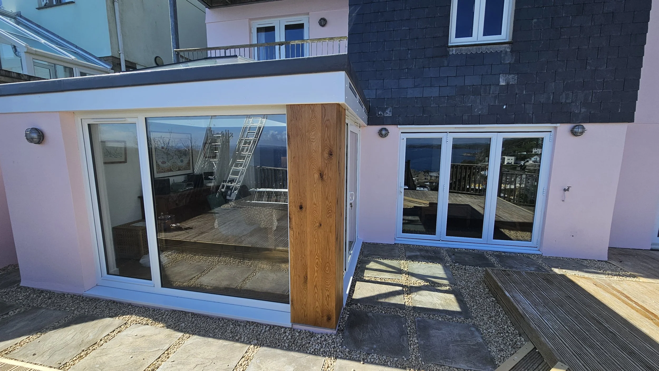 View of a house patio with sliding glass doors, wooden accents, and deck stairs overlooking a body of water.