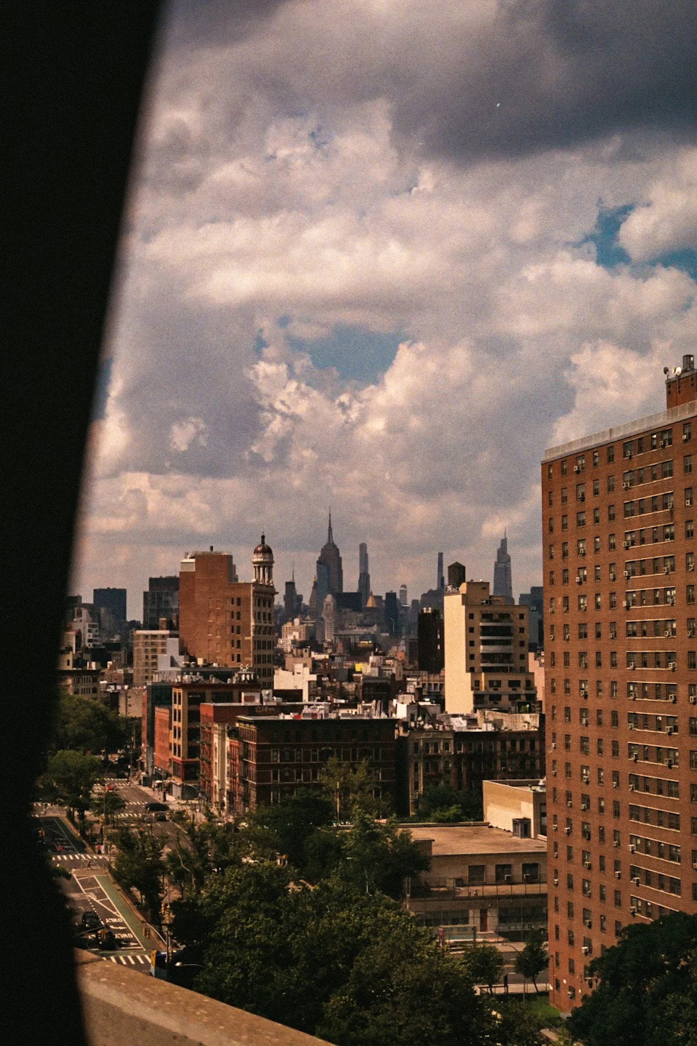 Cityscape of New York City with skyline, including the Empire State Building and other skyscrapers, seen through a partially opened window on a cloudy day.