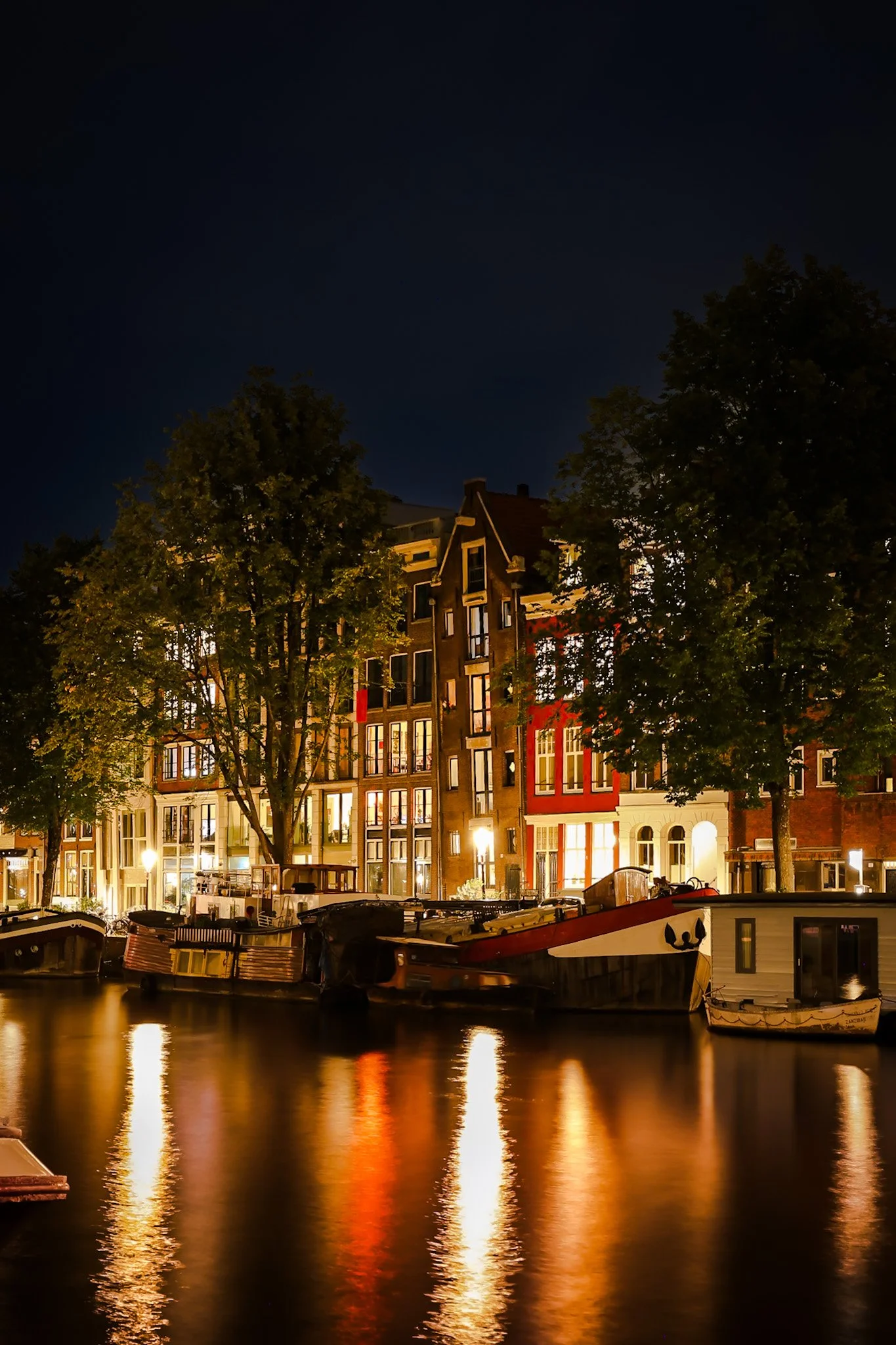 Night view of houses and boats along a canal with reflections on the water.