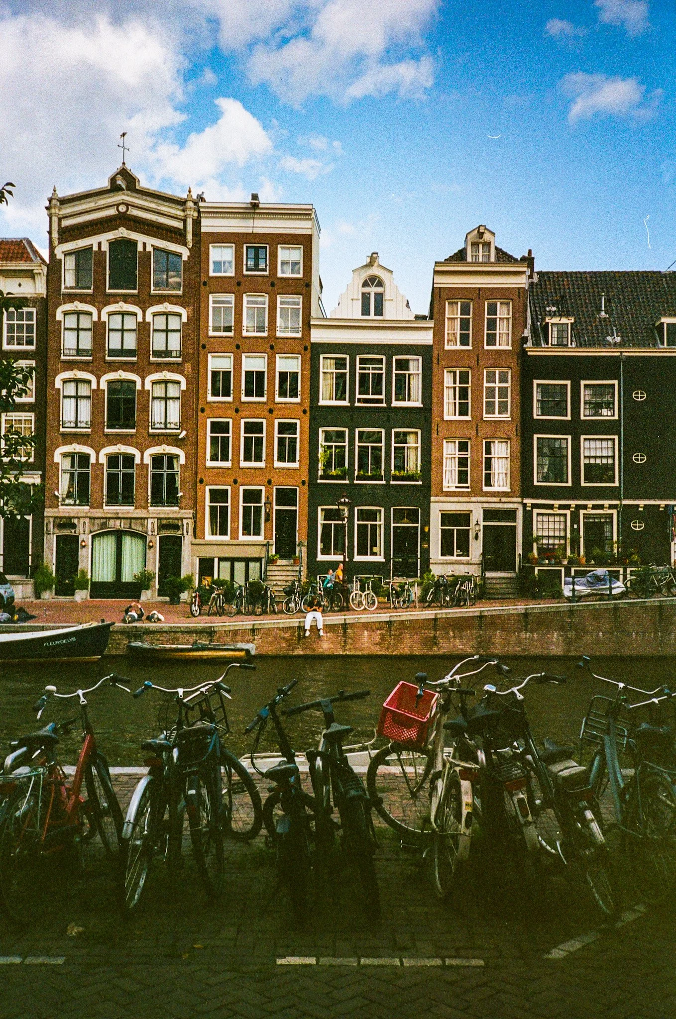 Bicycles parked along a canal in front of colorful traditional European buildings under a blue sky.