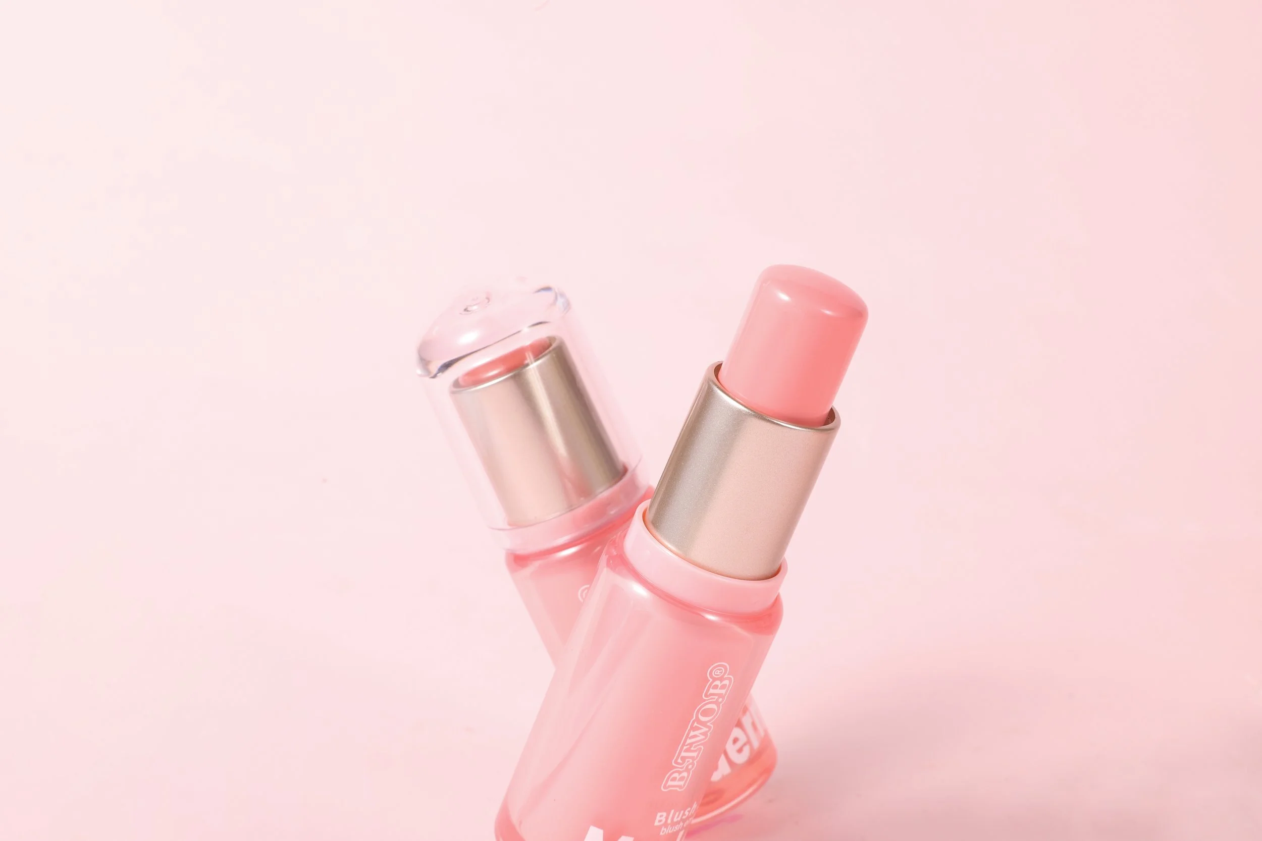 Baton de batom rosa em estojo de cor rosa claro com detalhes em prata, sobre fundo rosa claro