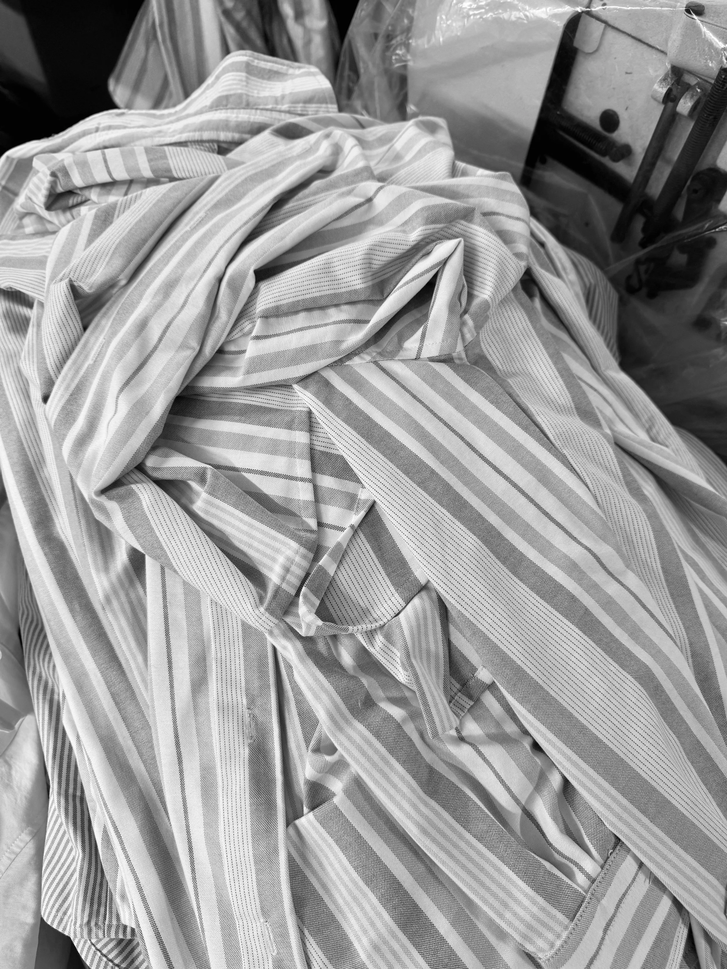 A pile of crumpled striped fabric, oxford cloth clothing, on a surface with workshop and haberdashery in the background.
