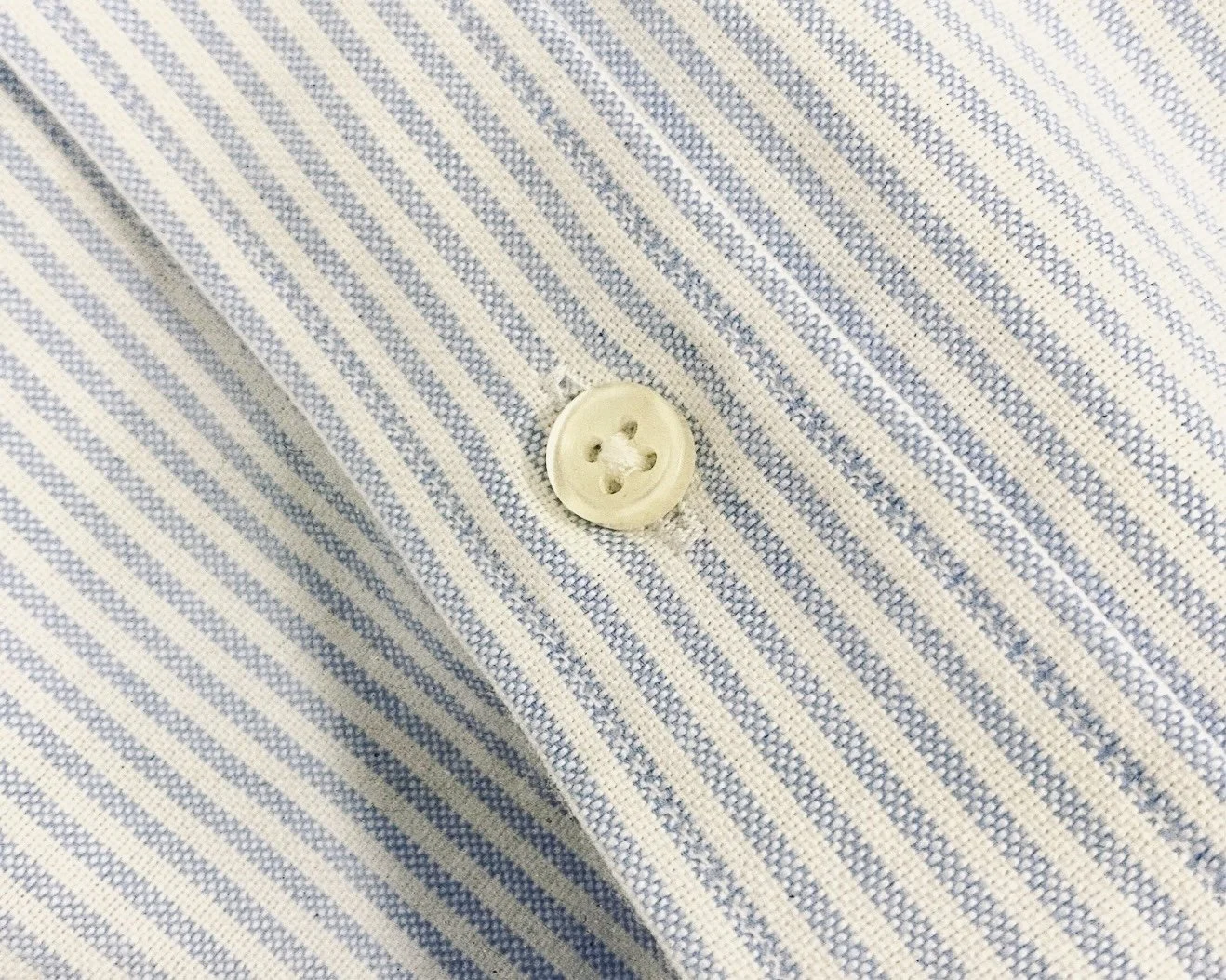 Close-up of a light-coloured oxford cloth fabric shirt with blue vertical stripes and a white button.