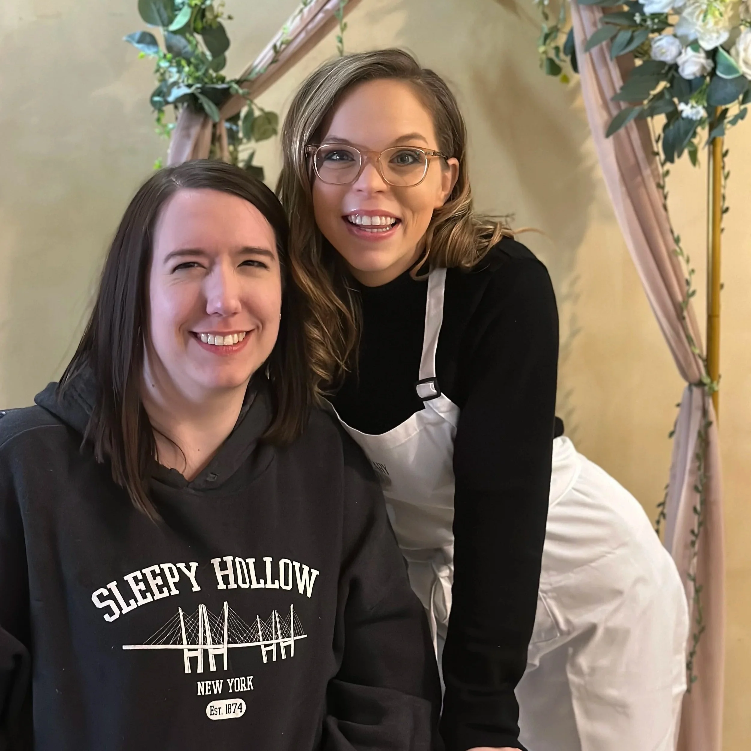 Two women smiling, one wearing a black hoodie with