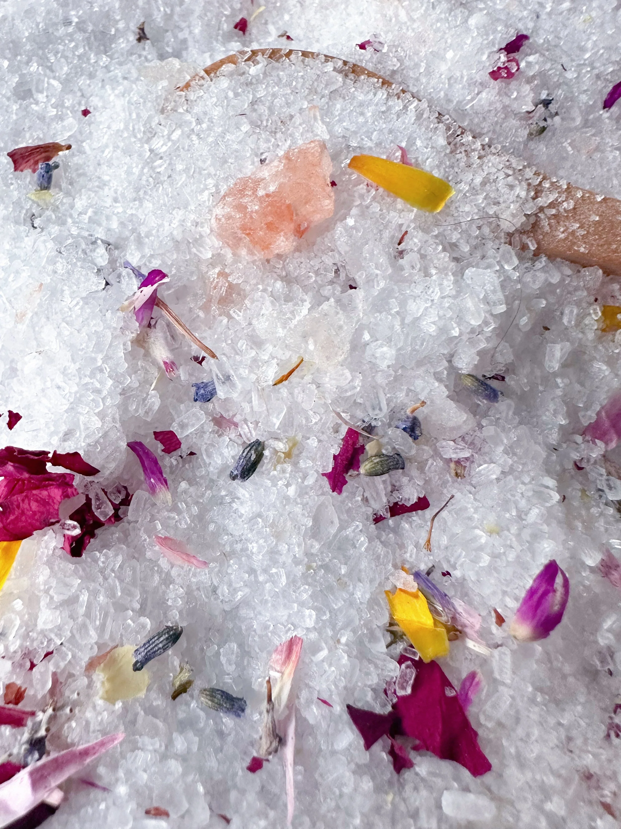 Close-up of coarse salt with colorful flower petals and a small pink Himalayan salt crystal.