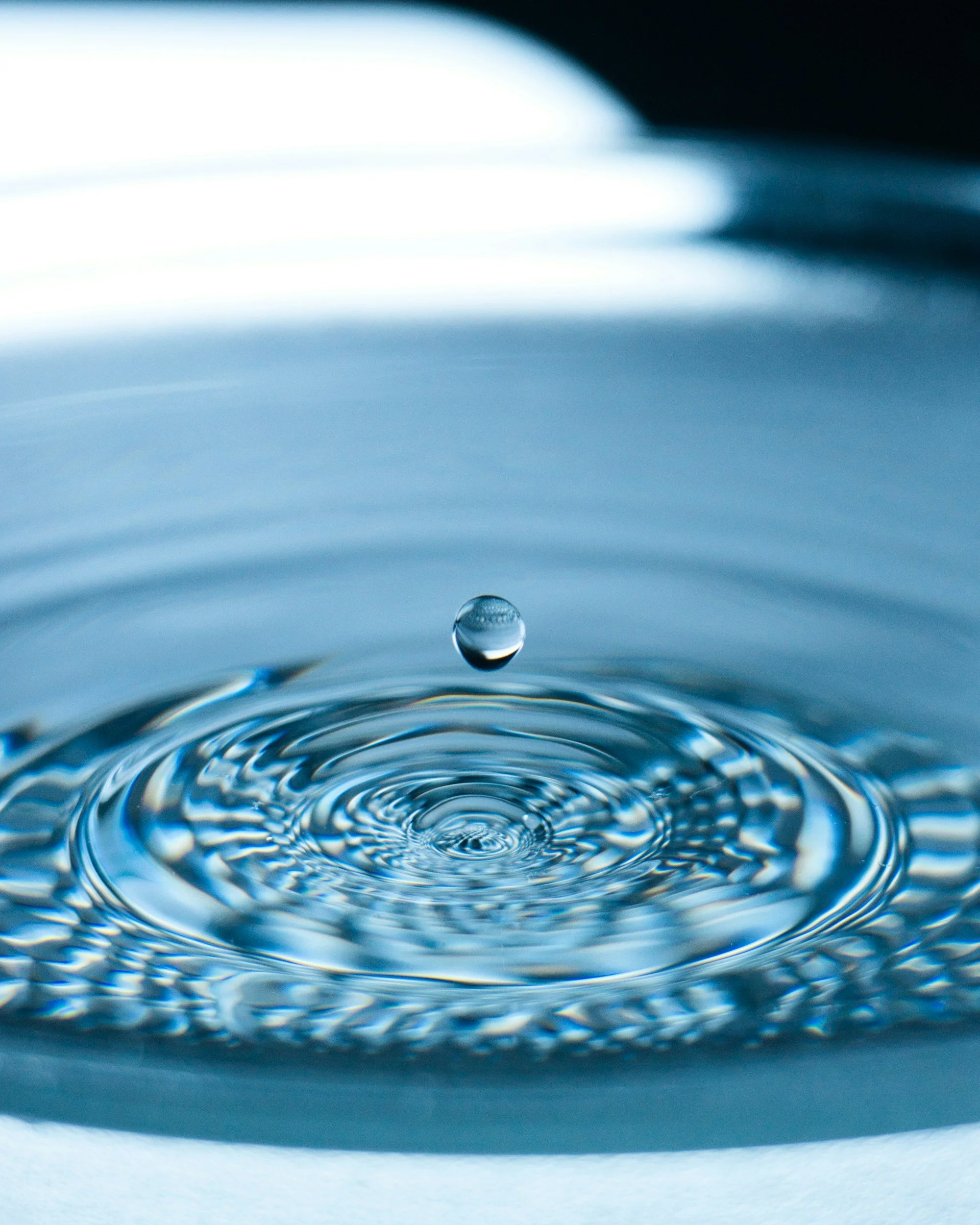 Close-up of a water droplet falling into a water surface, creating ripples.