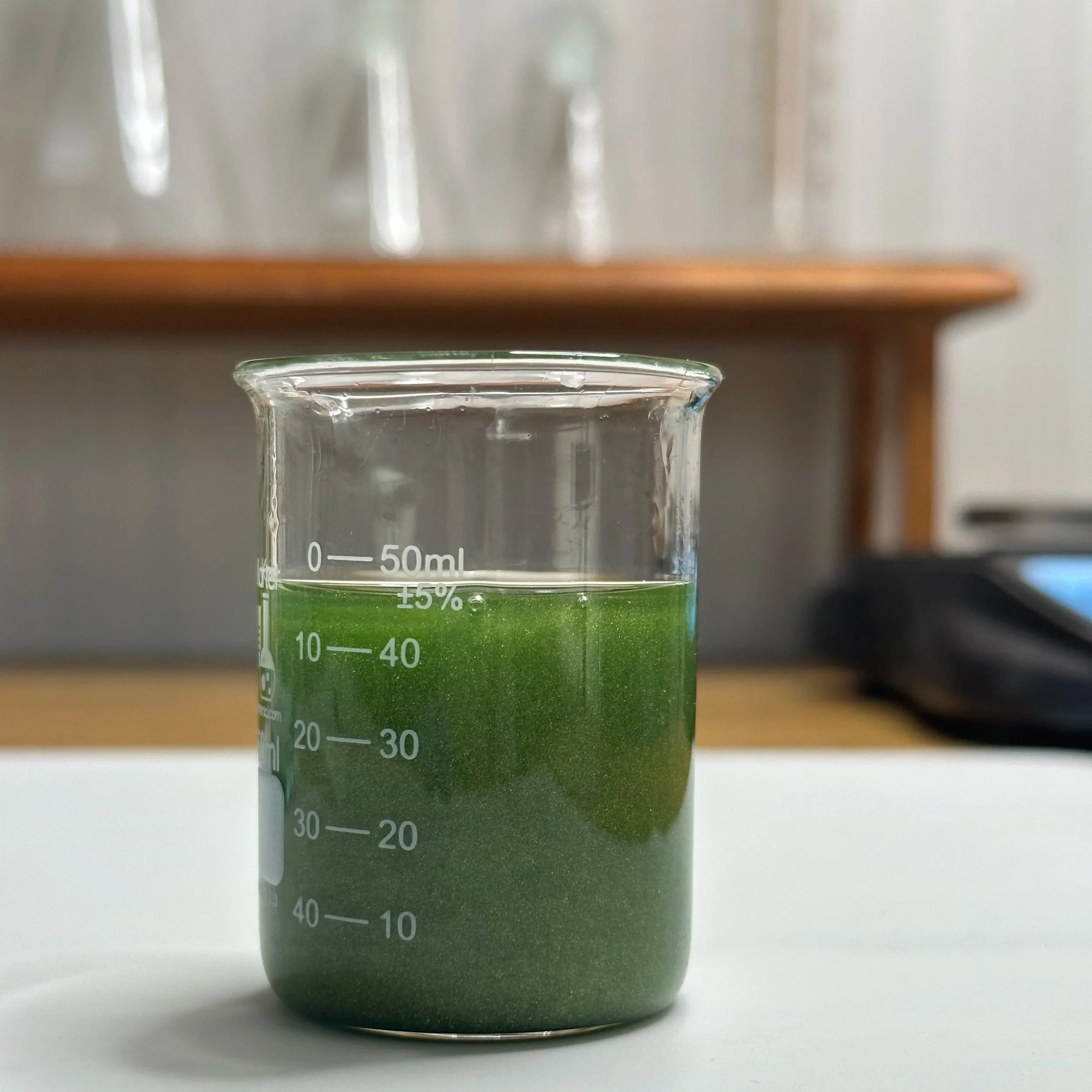 A laboratory beaker filled with a green liquid, placed on a white surface with a blurred background.