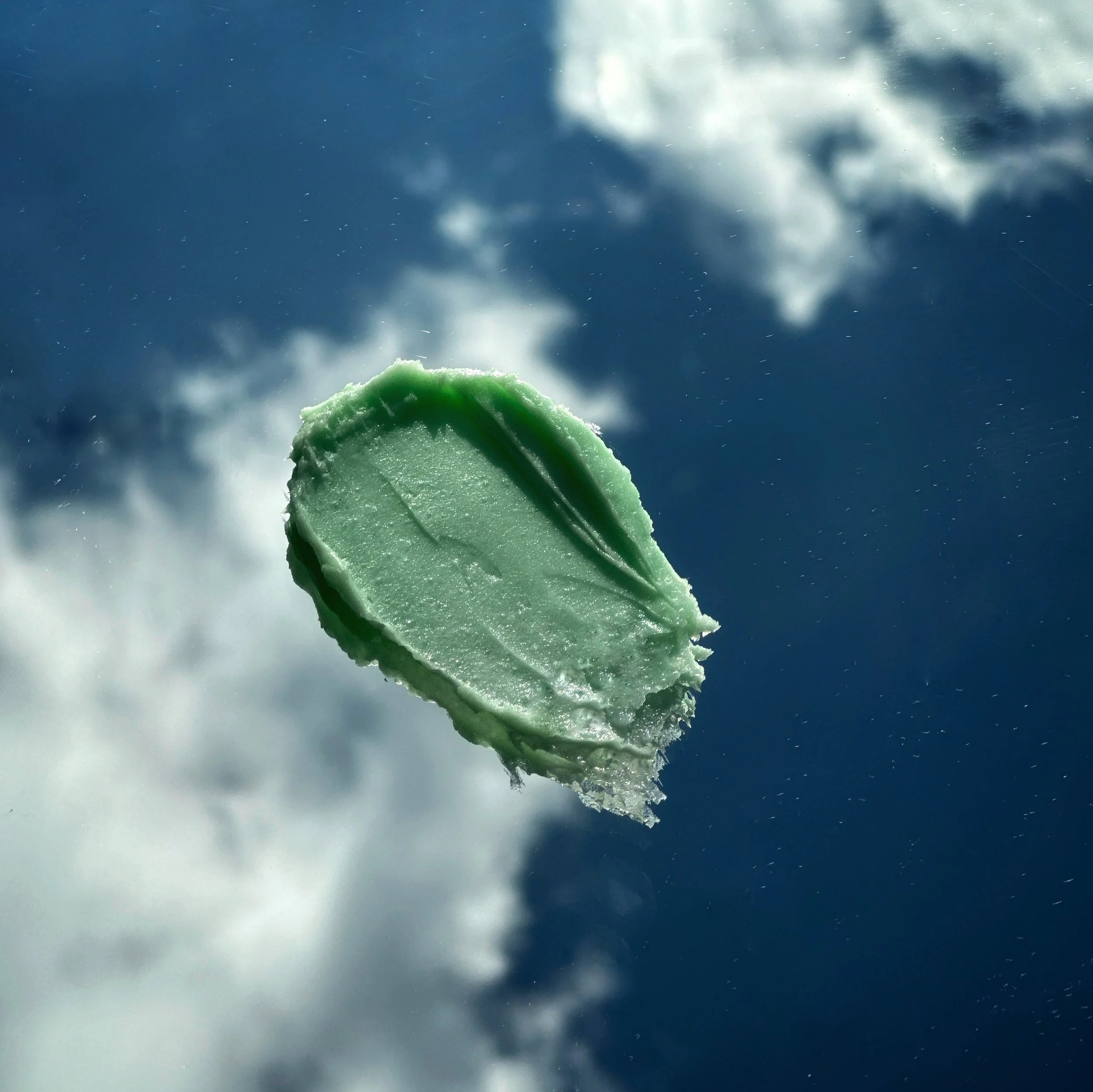 A green ice cream bar melting in the sky with clouds in the background.