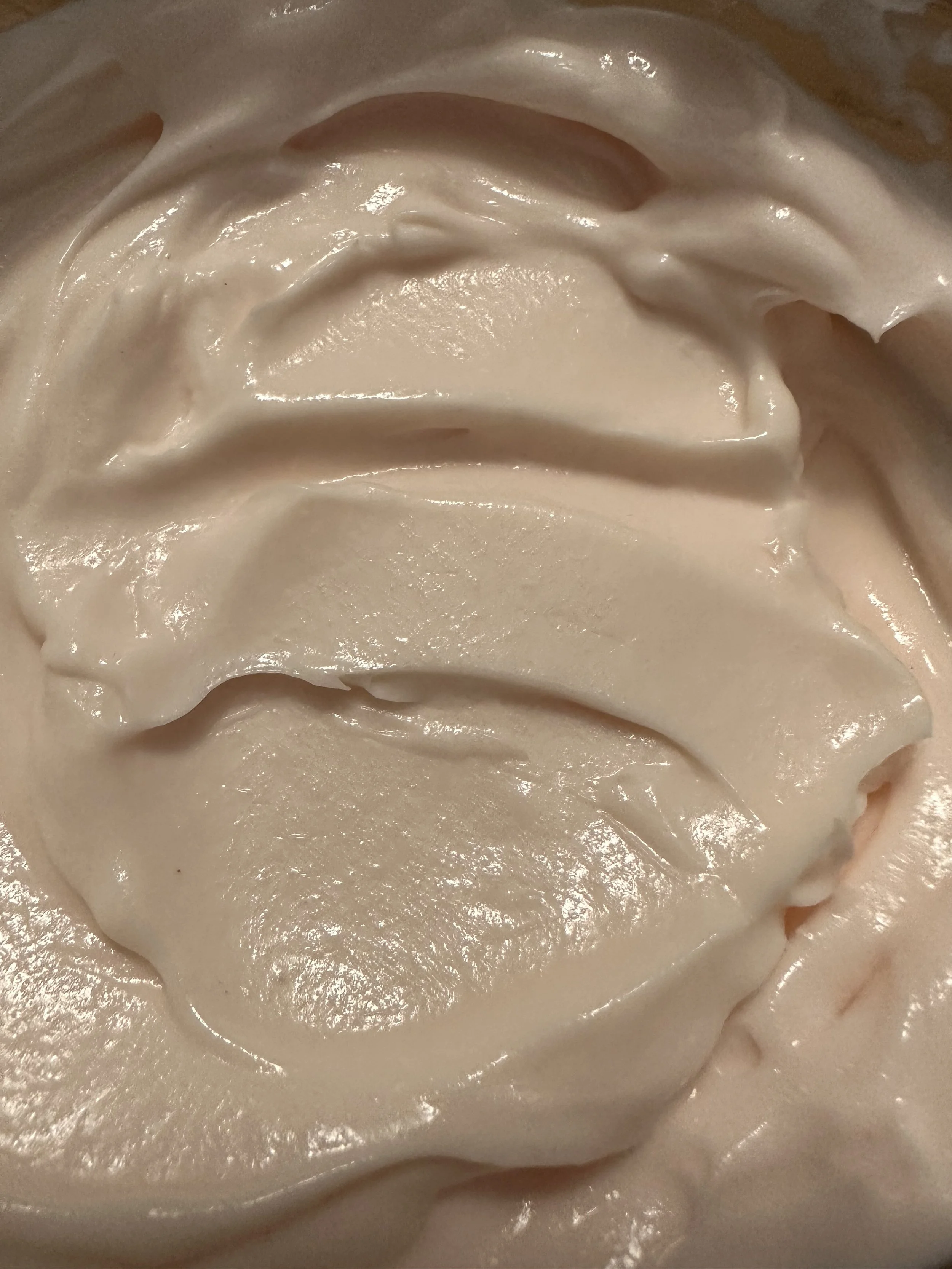 Close-up of smooth, creamy, light-colored frosting or whipped cream with a glossy texture.