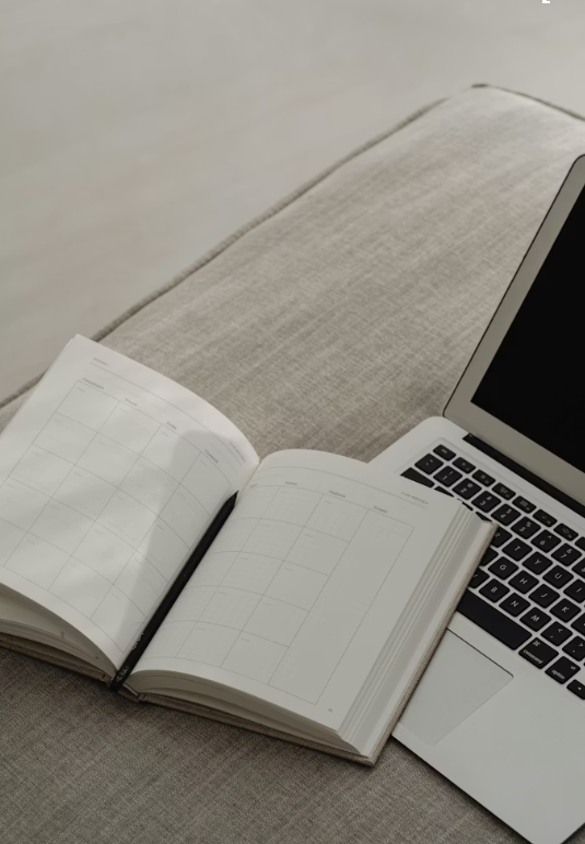 Open planner and silver laptop resting on light gray fabric surface.