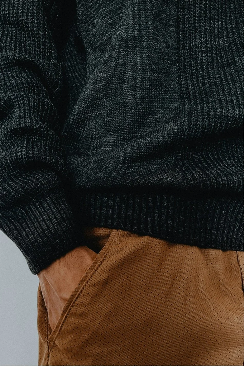 Close-up of a person's midsection showing a dark gray sweater and tan pants with a textured pattern.