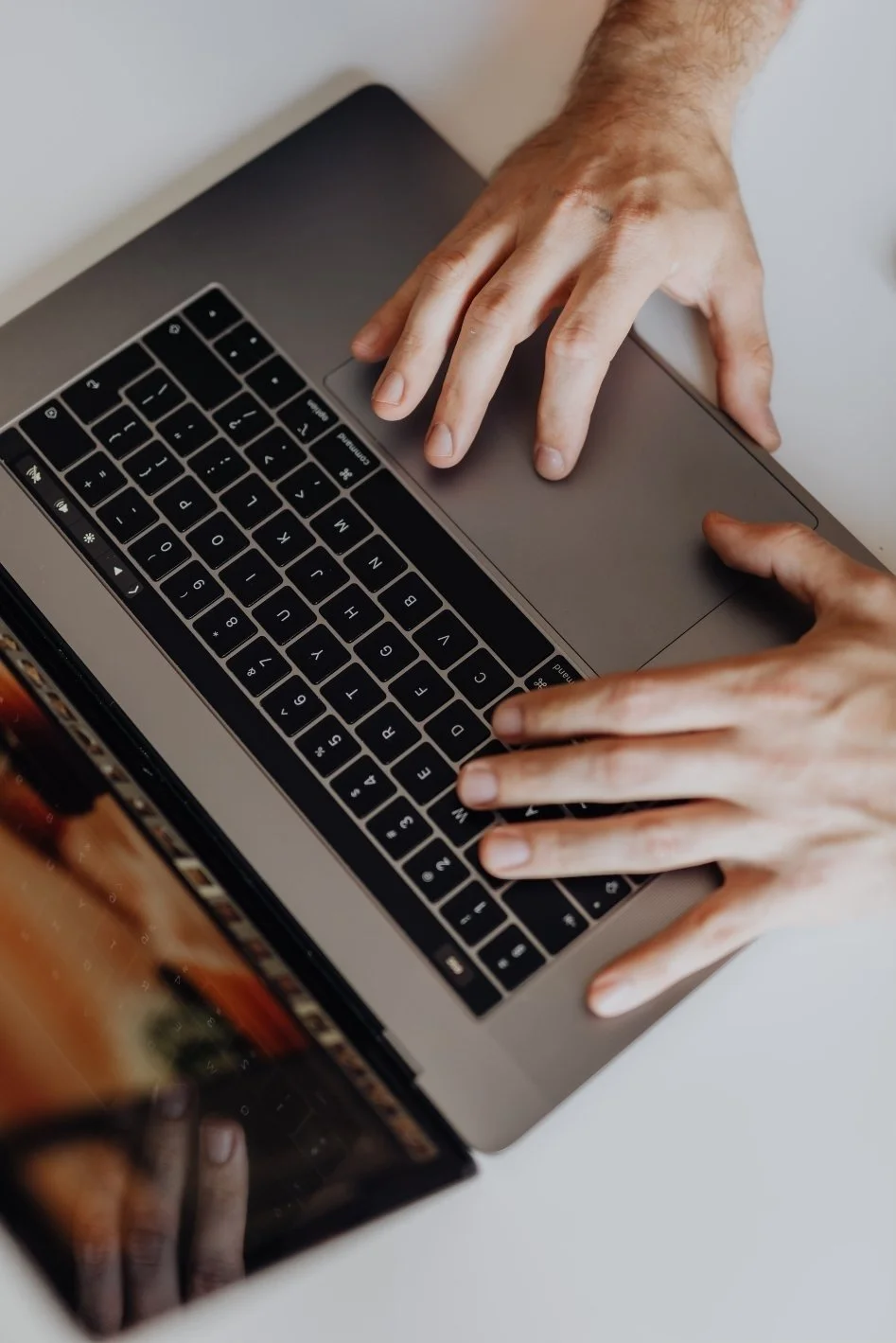Hands typing on a laptop keyboard with a touchpad.