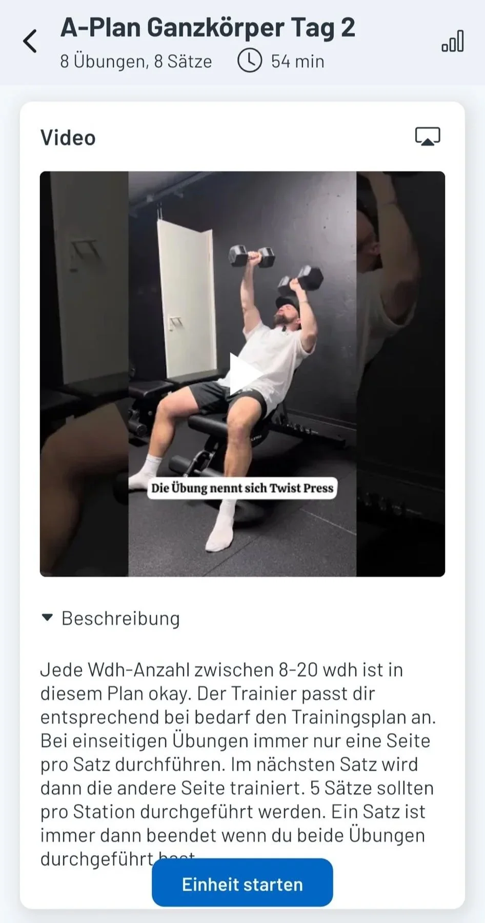 Ein Mann liegt auf einer Trainingsbank im Fitnessstudio und hebt mit beiden Händen Hanteln über dem Kopf. Er trägt ein weißes T-Shirt, schwarze Shorts, weiße Socken und eine schwarze Mütze.