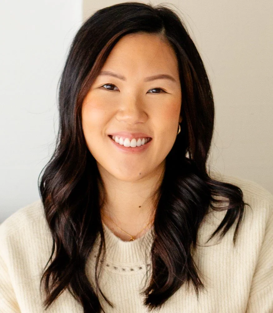 A therapist in Oklahoma City with dark brown hair wearing a light ivory sweater, thin gold necklace, and smiling.