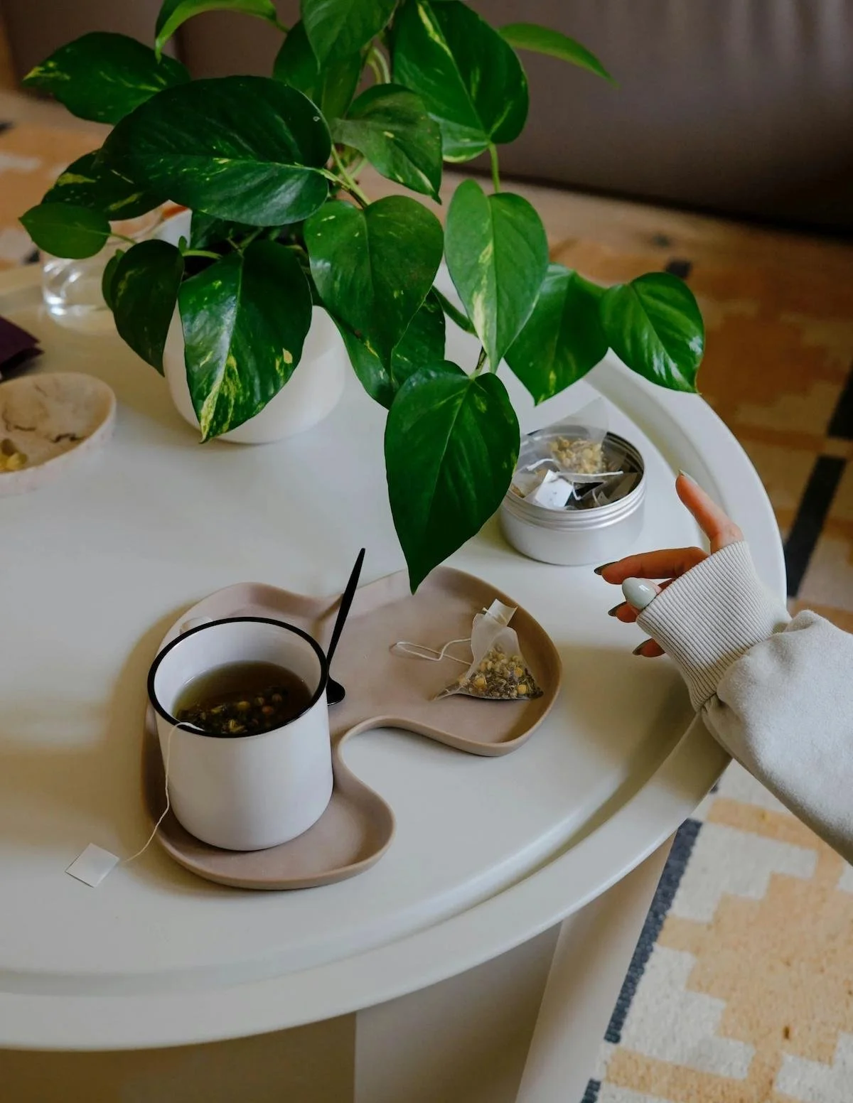 A cup of tea placed on a cream round table with a green pothos plant in the top left corner.