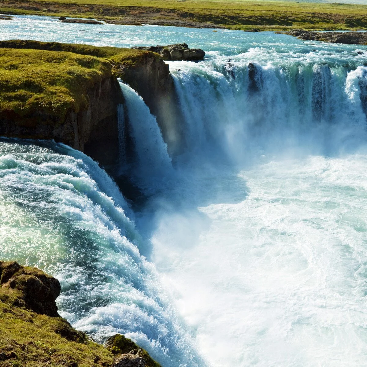 Waterfall cascading over cliffs with green grassy land in the background.