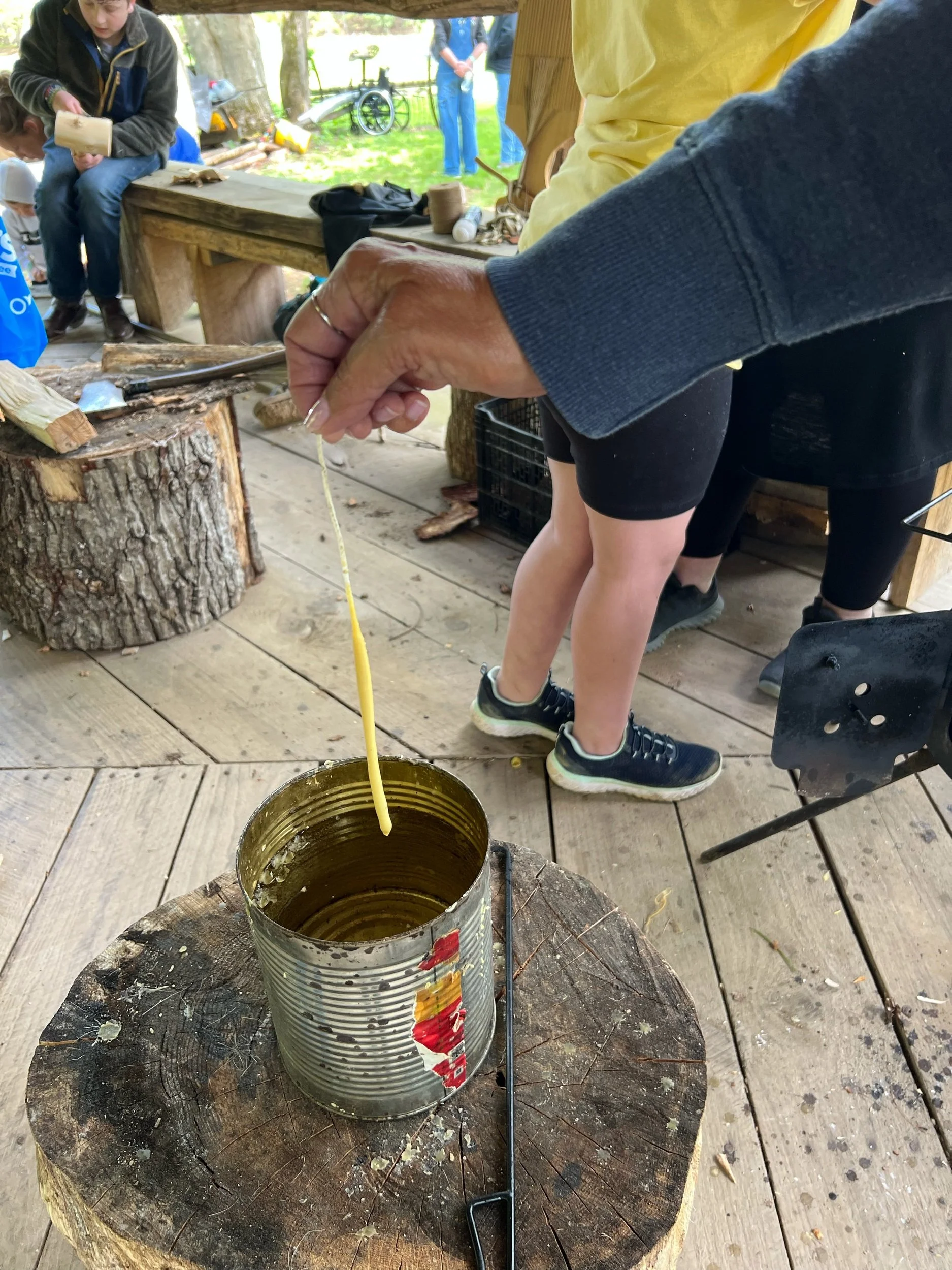 Person holding a string of cheese over an open can with a wooded table and children in the background