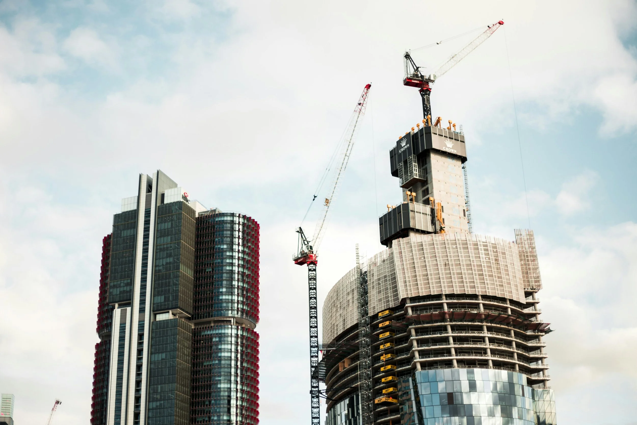 Under construction skyscraper with two cranes against partly cloudy sky.