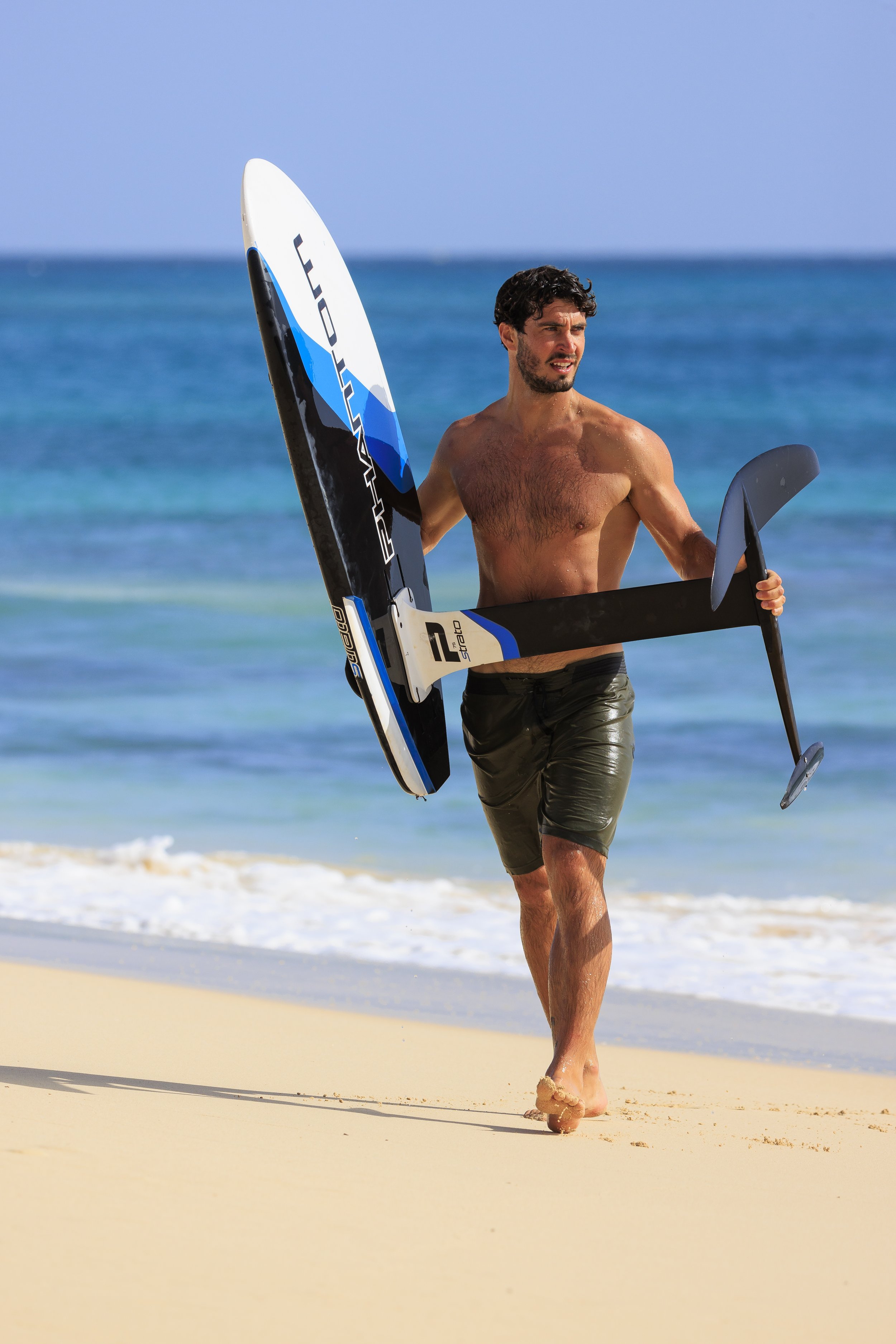 Man carrying hydrofoil surfboard on beach with ocean background
