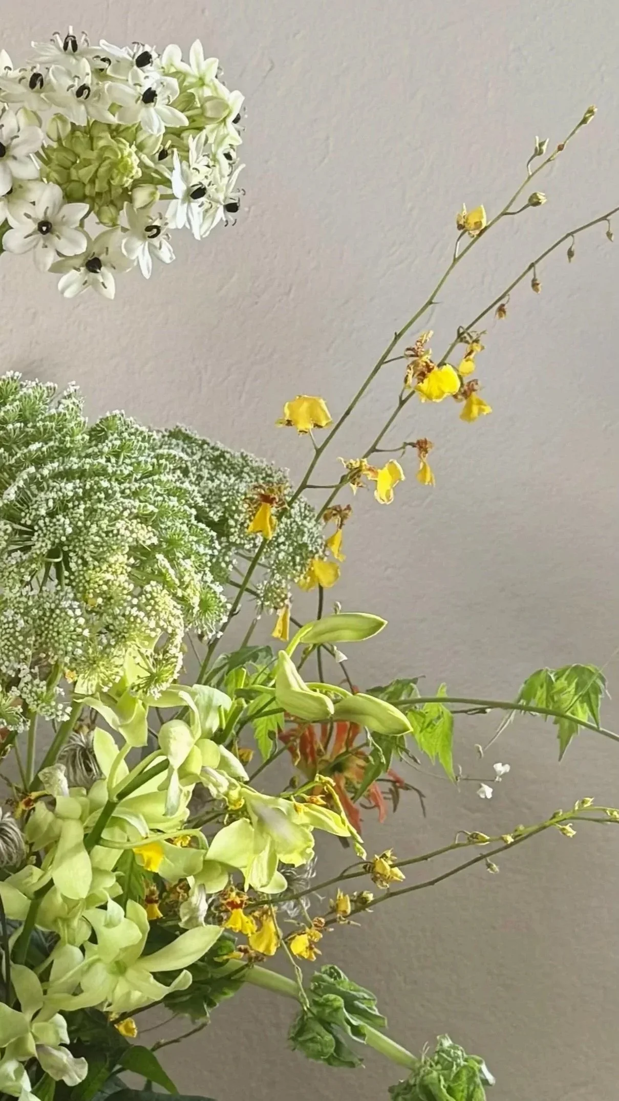 Arrangement of various flowers including white, green, and yellow blooms against a plain background.