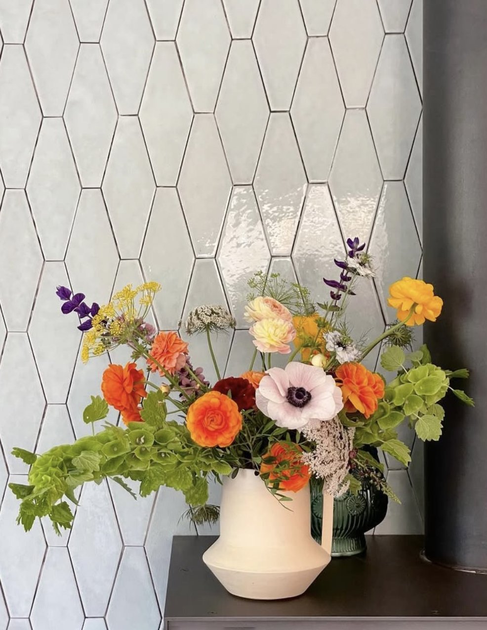 A colorful bouquet of flowers in a white vase on a dark table with a white honeycomb-patterned wall in the background.