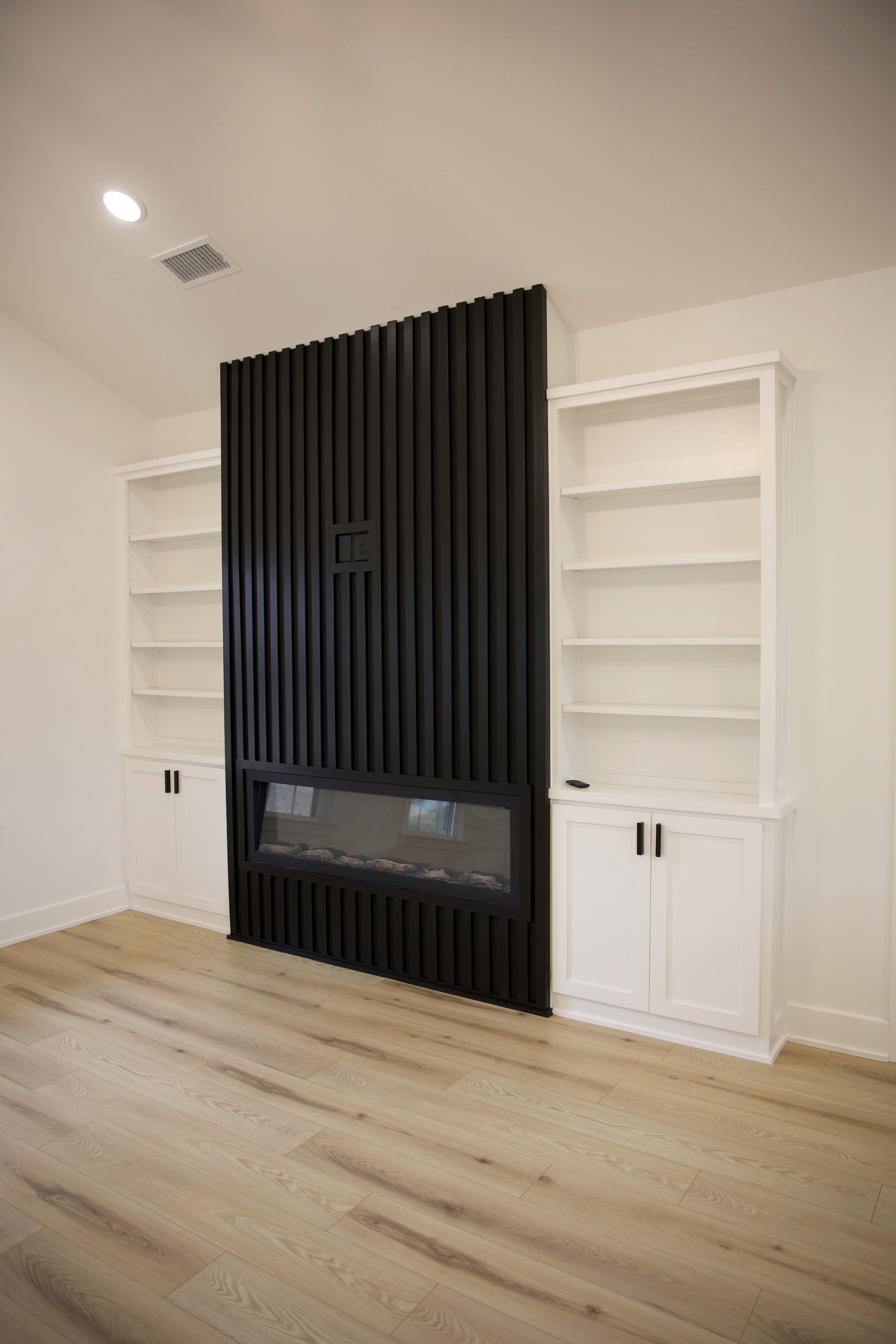 Living room with built-in white bookshelves on either side of a black accent wall with vertical slats and an electric fireplace.