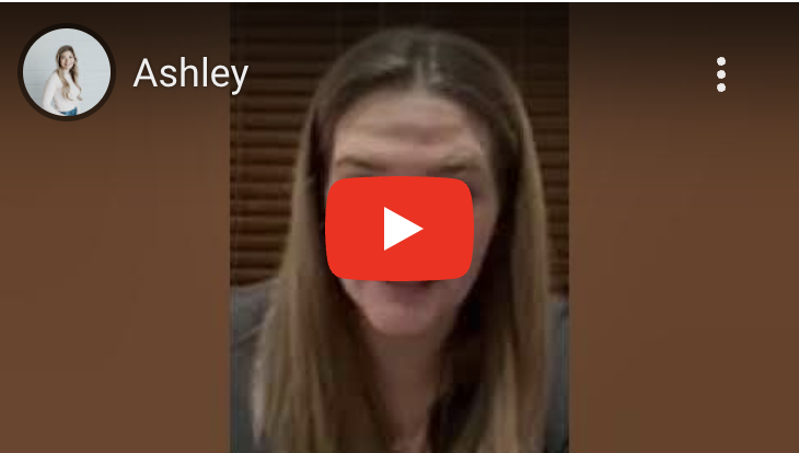 A woman with long brown hair making a funny face, with her tongue sticking out, in a casual indoor setting.