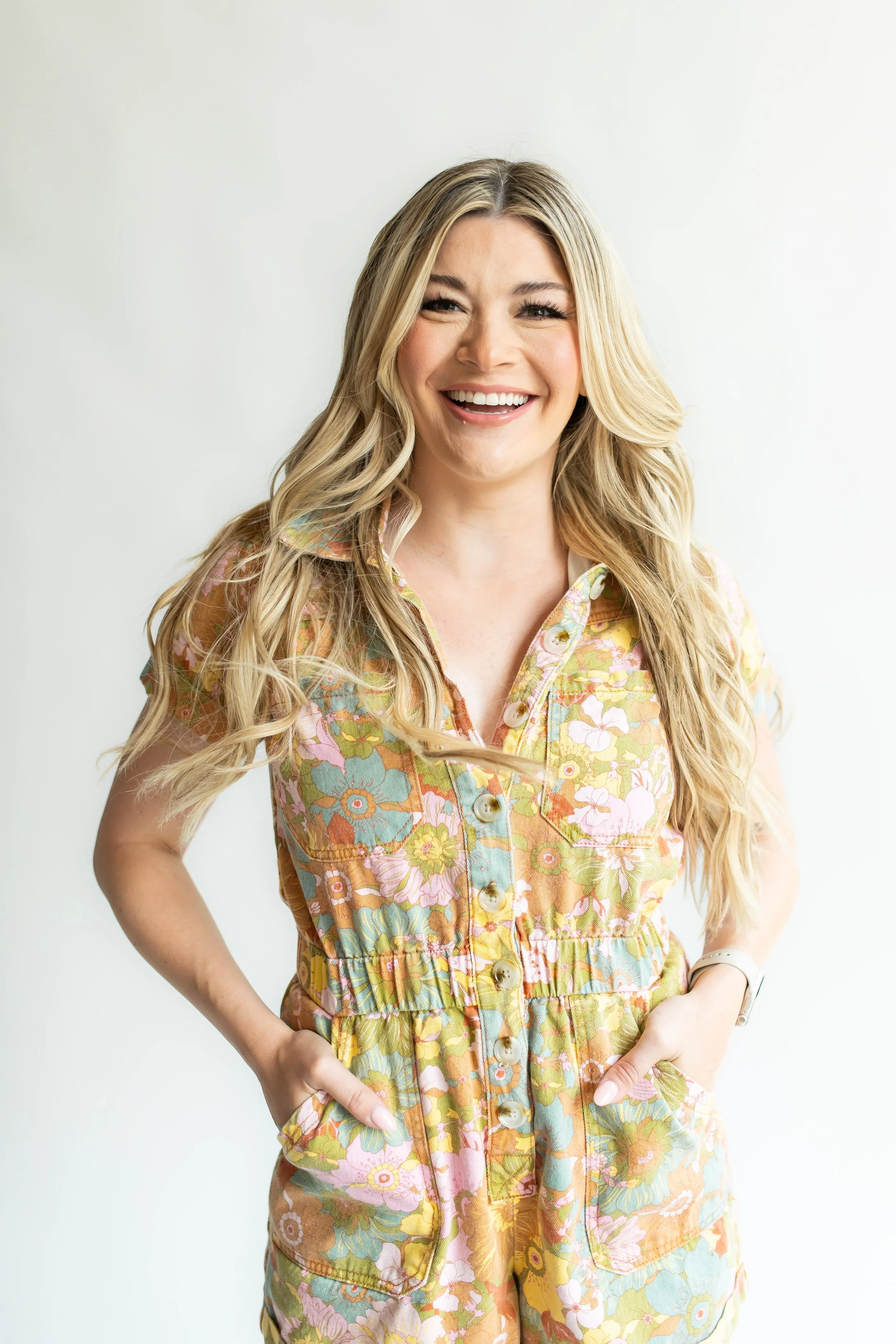 Haley in colorful floral jumpsuit and posing with her hands in her pockets.