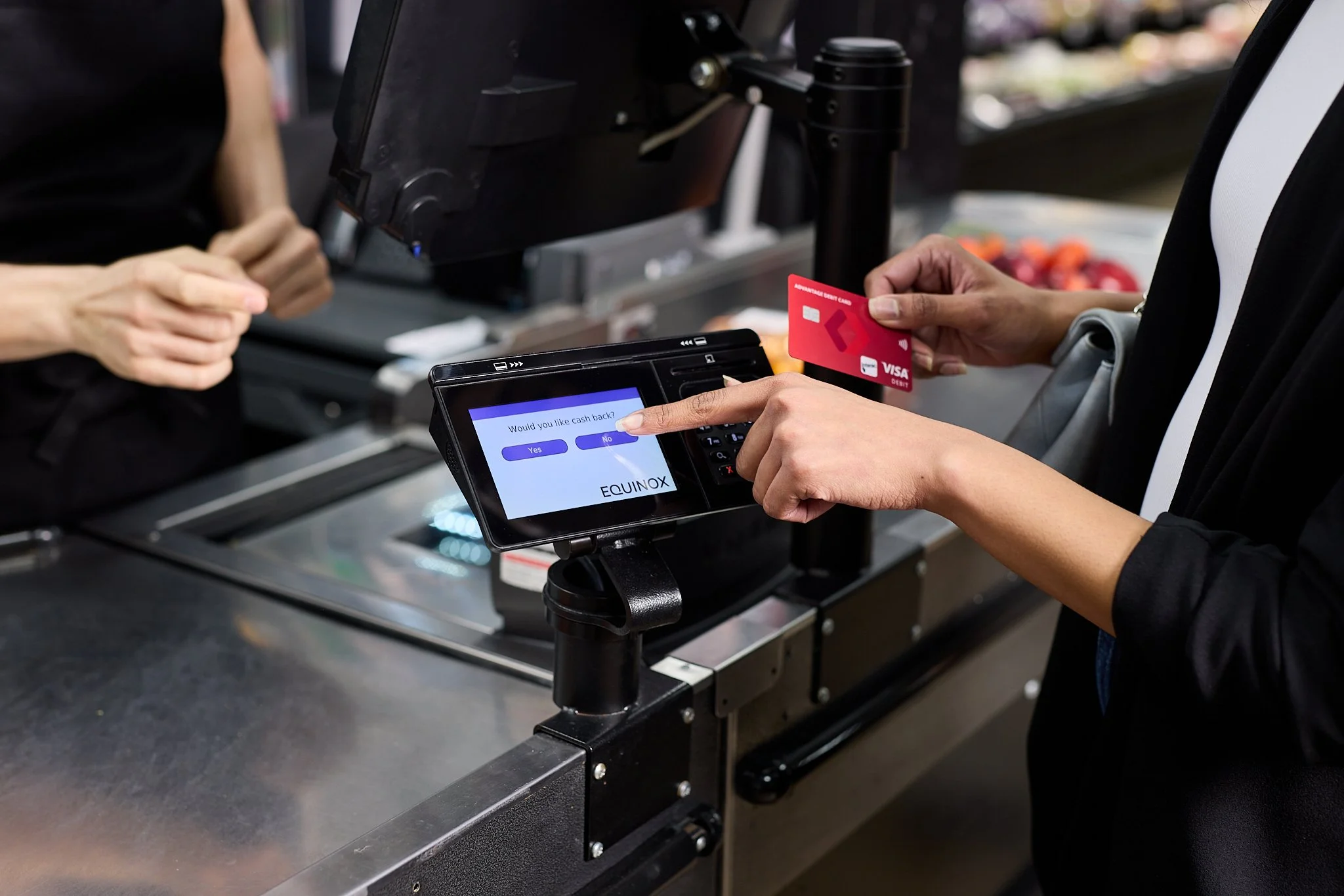 Customer paying with credit card at checkout counter with a digital payment device and ask 'Would you like cash back?' on screen.