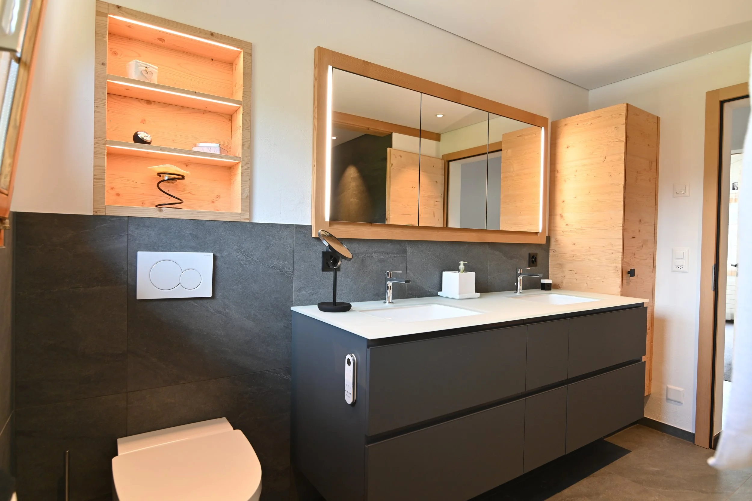 Moderner Badezimmer mit Doppelwaschbecken, Spiegel mit LED-Beleuchtung, dunklem Unterschrank, Holzregal mit LED-Beleuchtung und Wischmopp