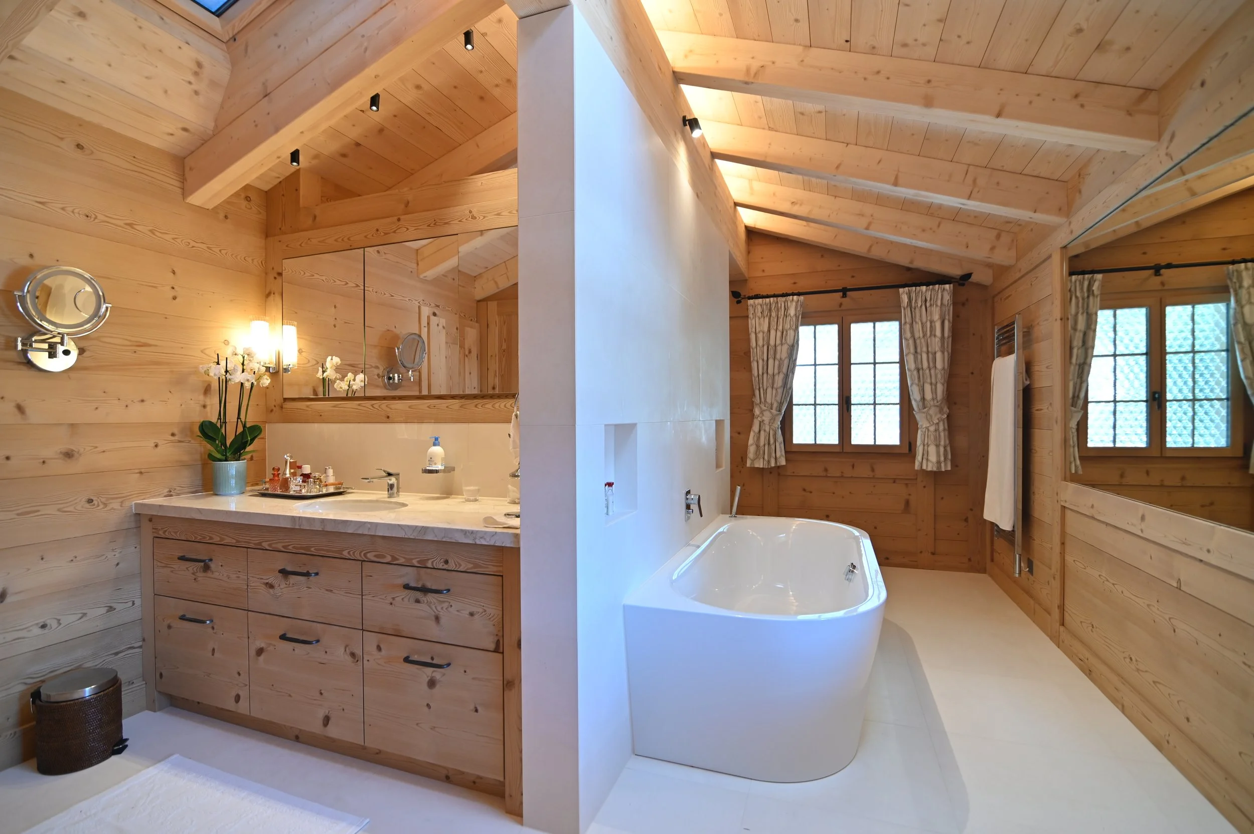 Holzverkleideter Badezimmerbereich mit Badewanne, Waschbecken und Spiegel, dekoriert mit einer Orchidee im Fenster