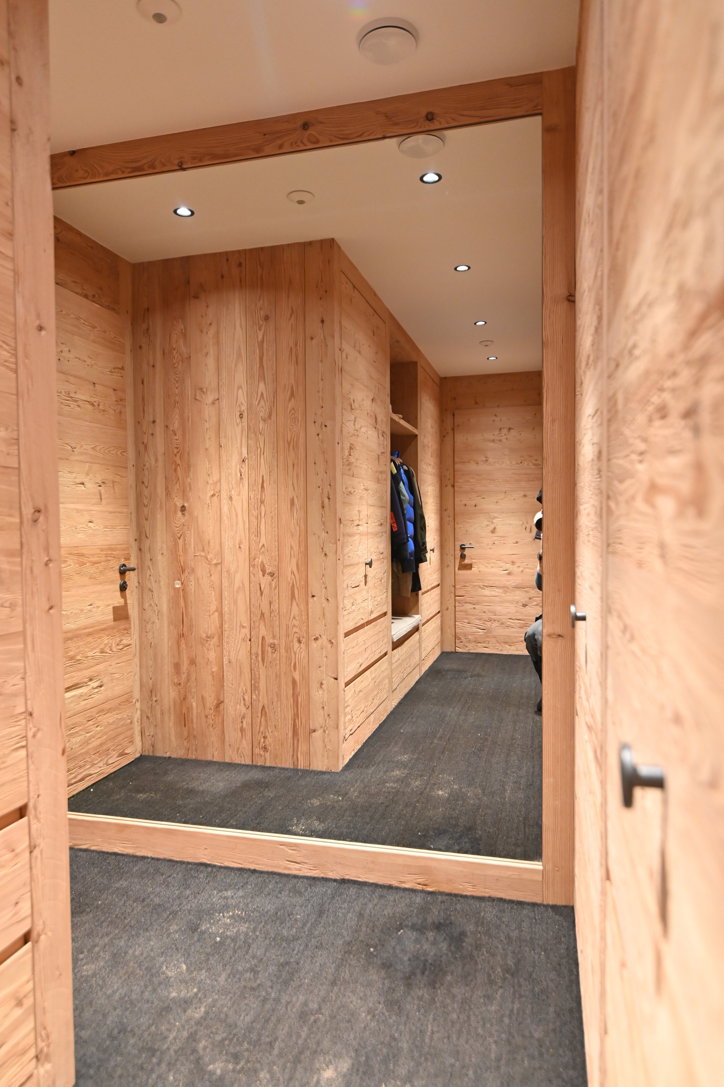Ein begehbarer Kleiderschrank mit Holzverkleidung, mehreren Halterungen für Kleidung und einem mit dunklem Teppich ausgelegten Boden.
