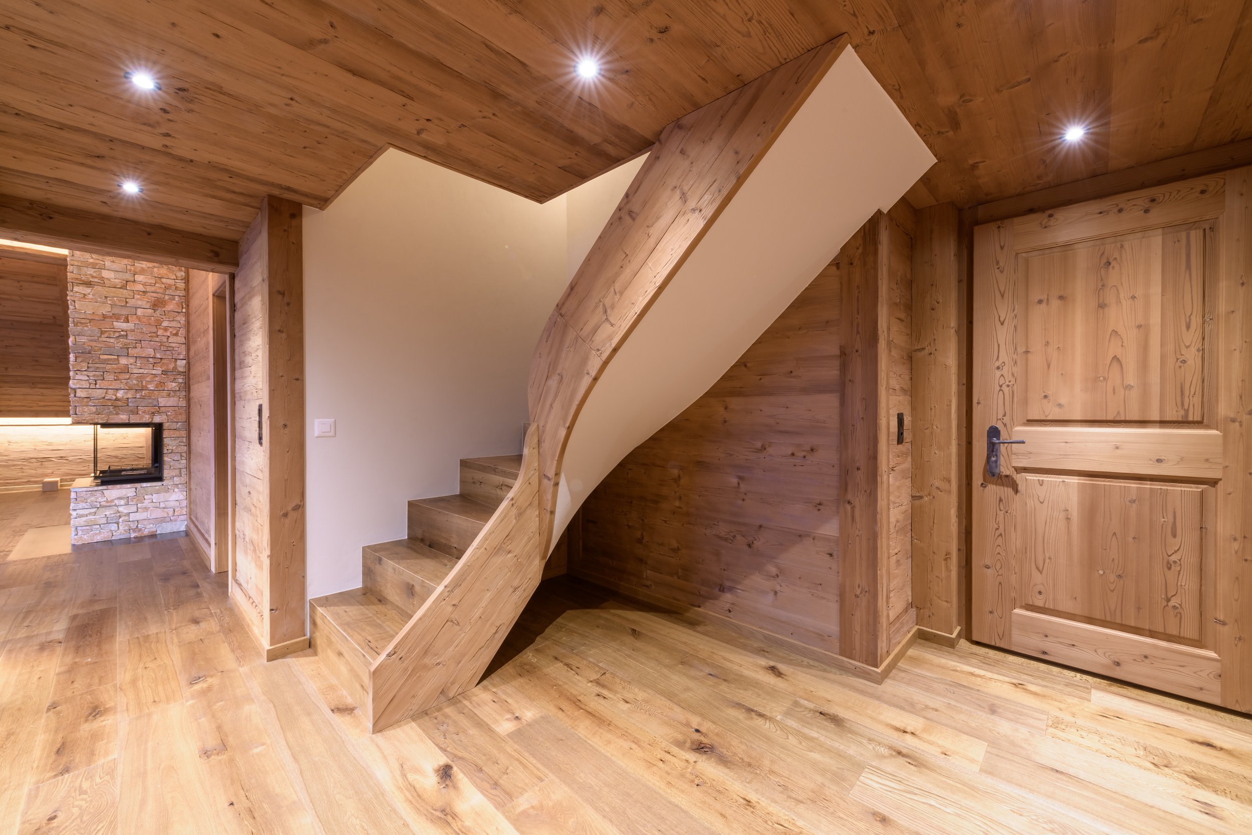 Innenaufnahme eines Holzhauses mit Treppe aus Holz und Holzvertäfelung an den Wänden, Deckenlichter und Holz-Tür.