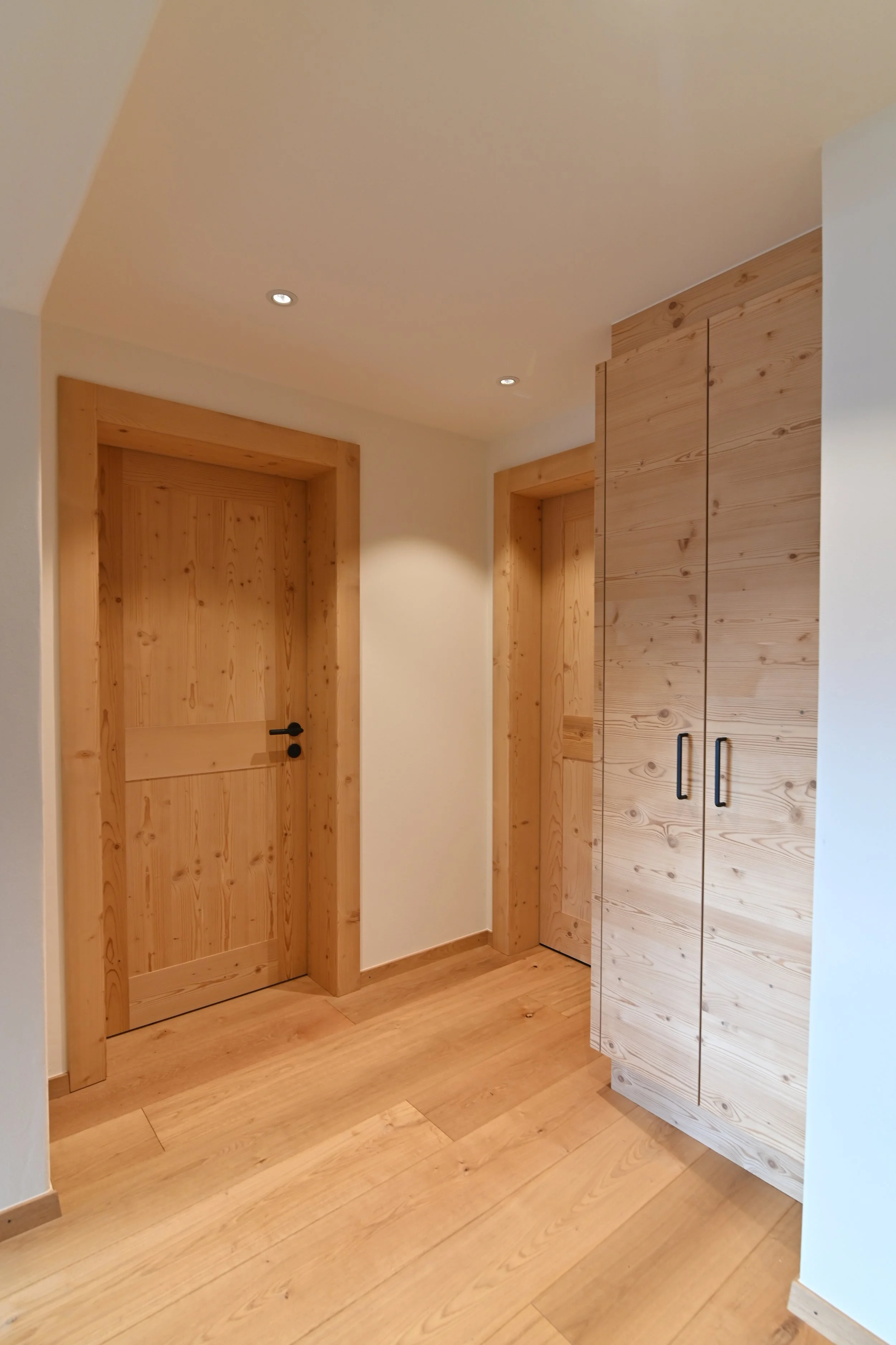 Ein Flur mit Holztreppen, Holztüren und Holzmöbeln, die warm beleuchtet sind.