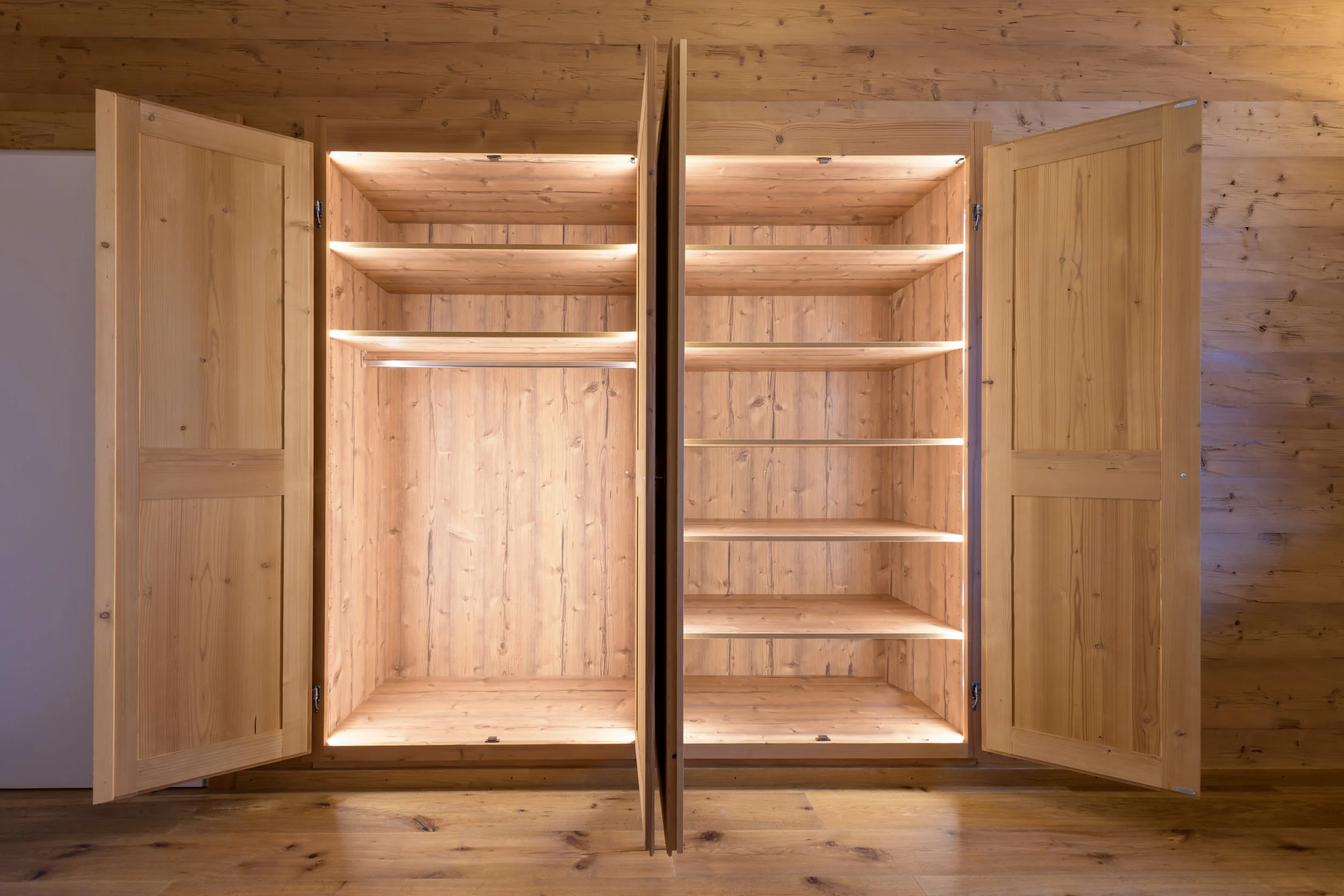 Offener Holzschrank mit vier offenen Regalböden, beleuchtet und aus massivem Holz gefertigt, vor Holzrahmen mit Holzvertäfelung.