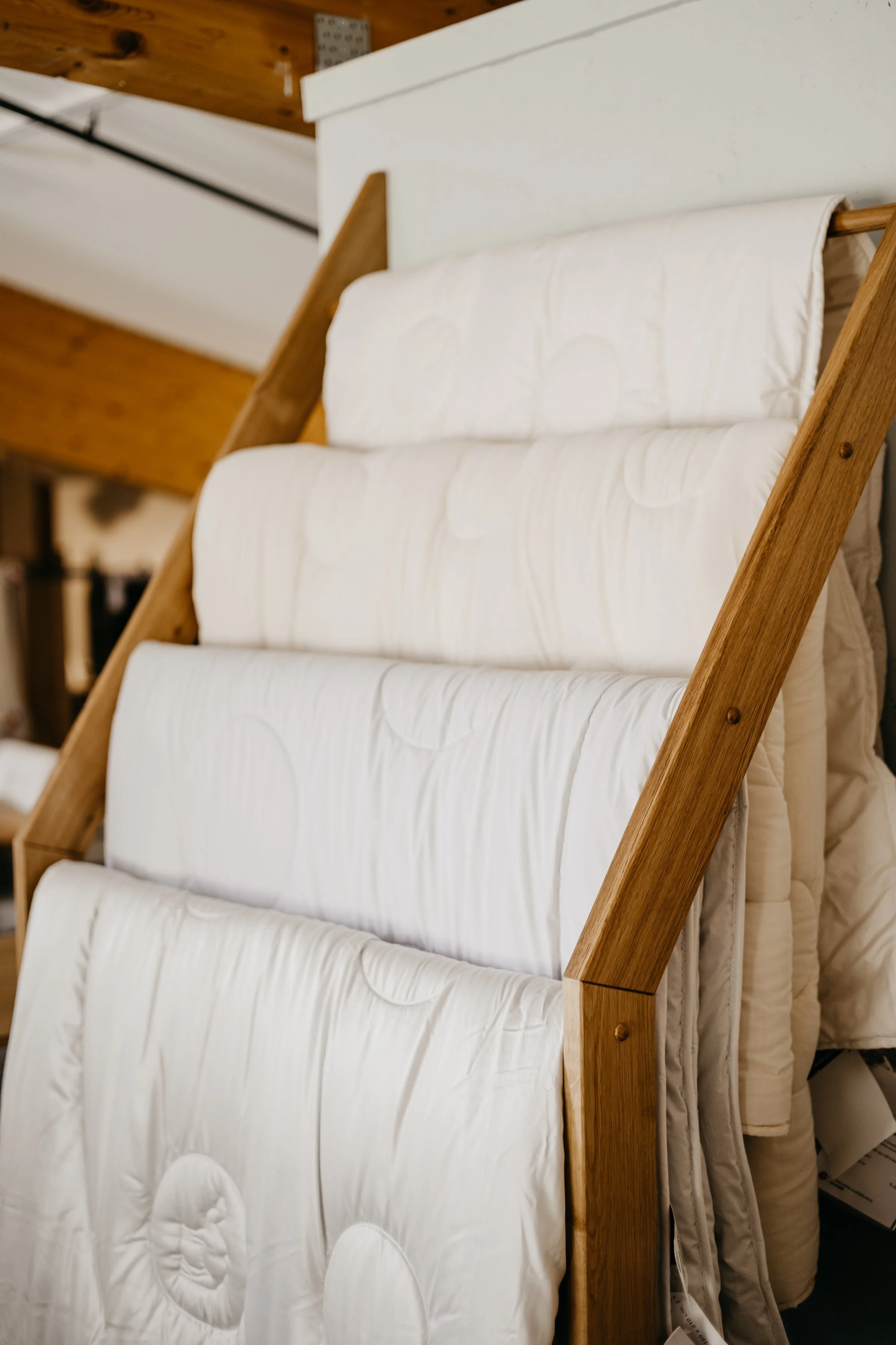 Mehrere weiße Matratzen mit Steppung, gestapelt an einem Holzrahmen in einem Raum mit Holzdecken und weißen Wänden.