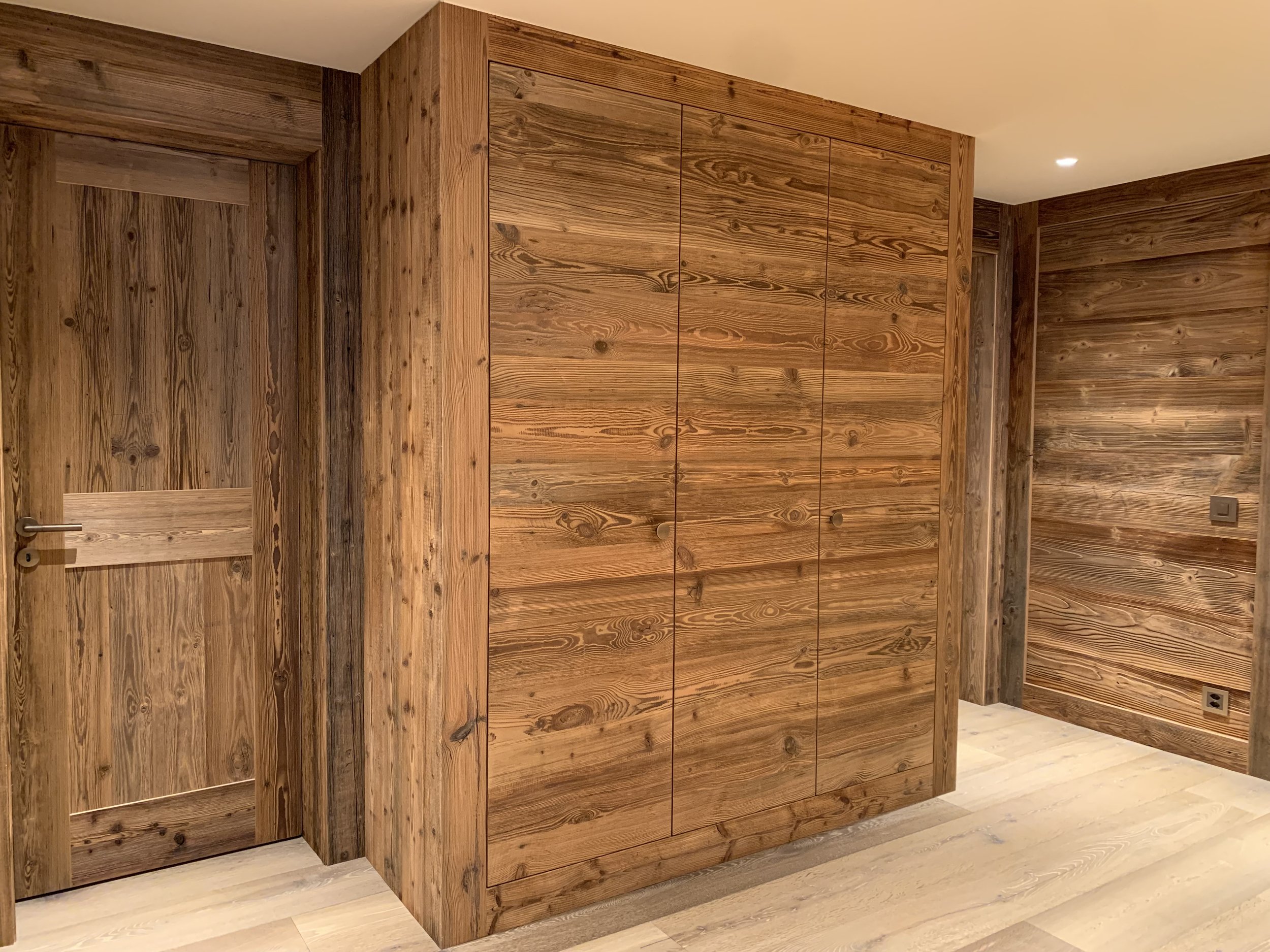 Holzverkleidung an einer Wand und an einer Tür in einem Raum, helle Holztöne, moderner Innenraum.