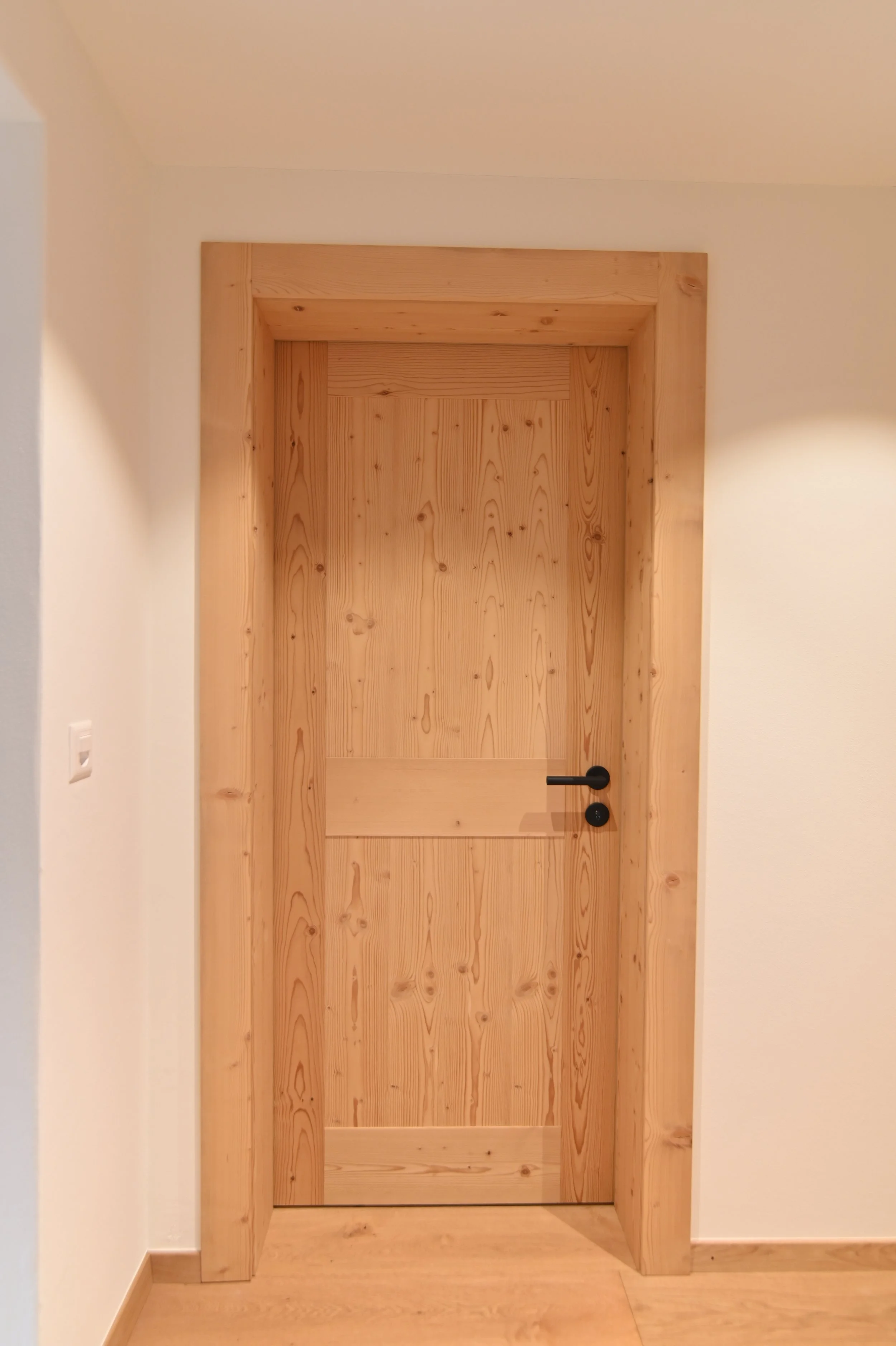 Holztür mit schwarzem Griff in einem Raum mit weißen Wänden und Holzboden.