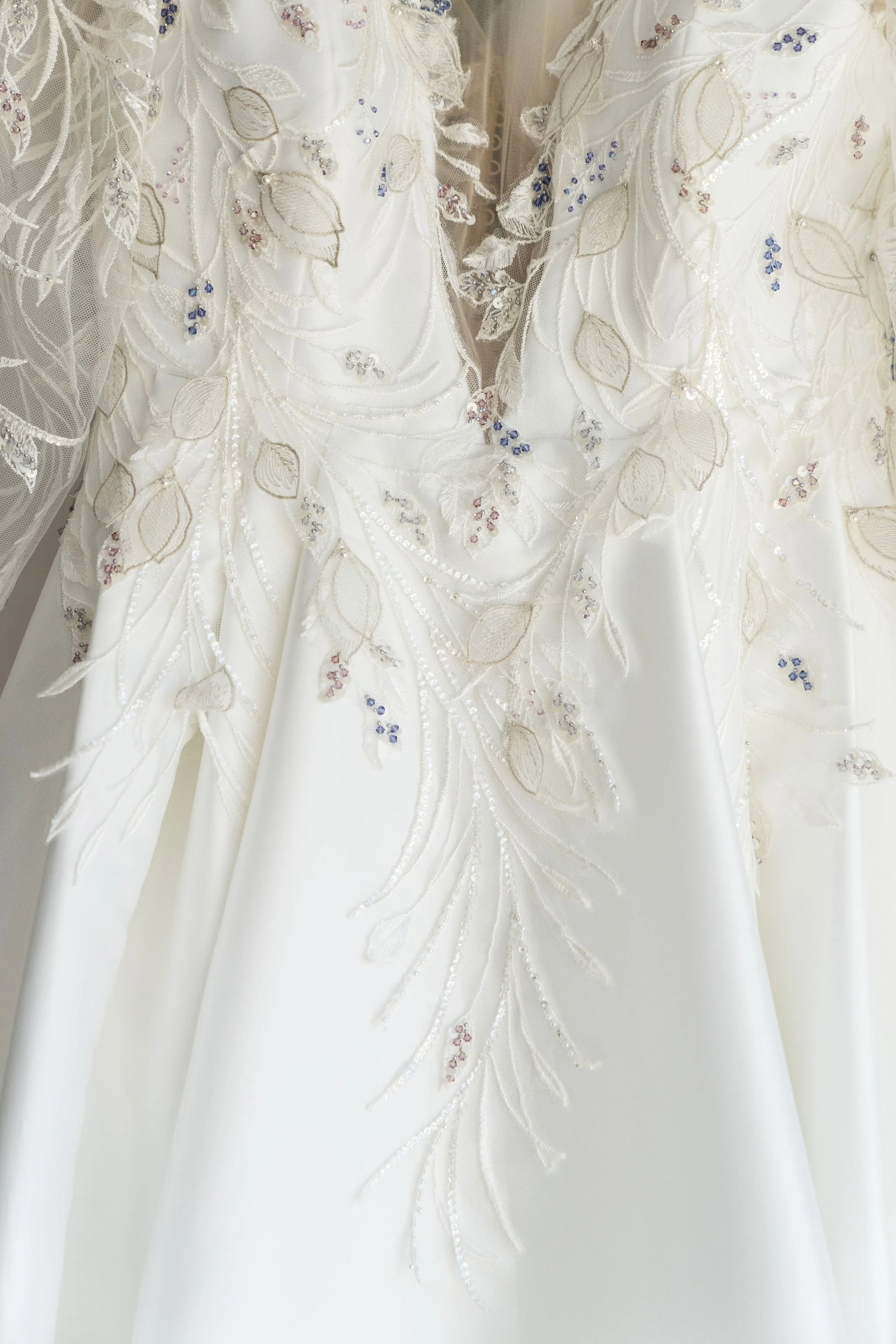 Close-up of a white wedding dress with embroidered leaves and flowers, adorned with small beads and sequins.